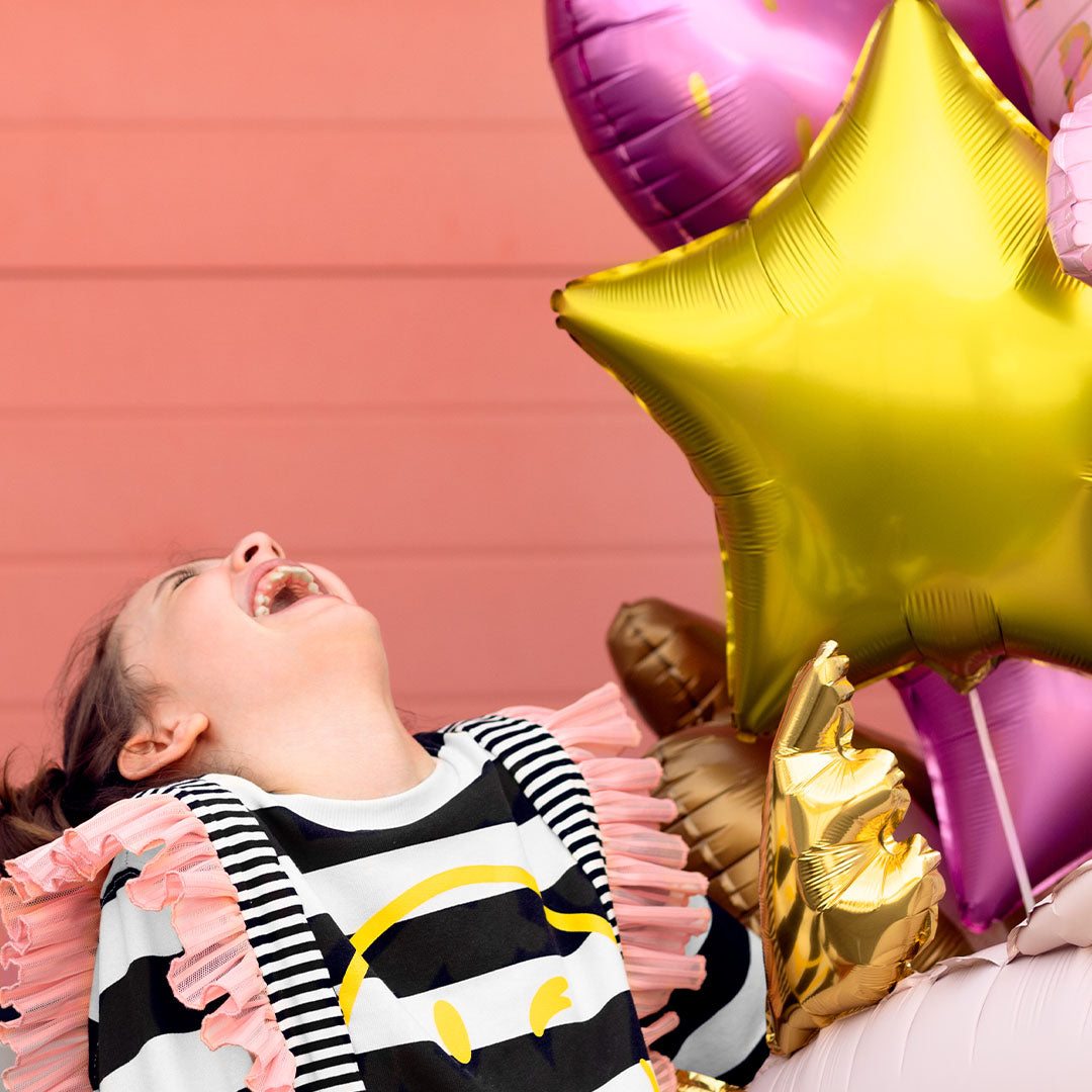 Lachend meisje kijkt omhoog naar een partydeco gouden ster folieballon en andere feestballonnen.