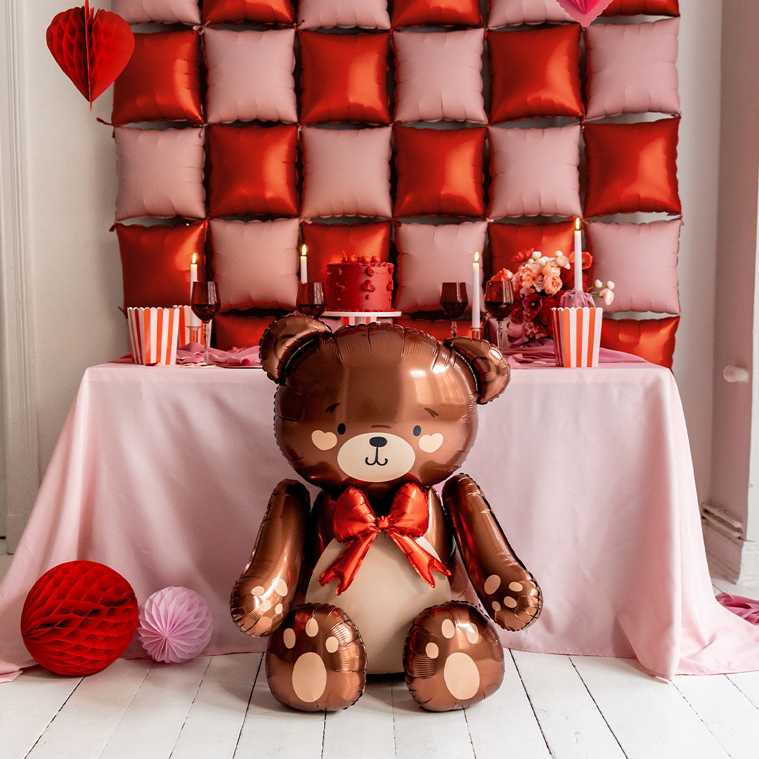 Partydeco folieballon in de vorm van een teddybeer als decoratie voor een feesttafel met roze en rode accenten.