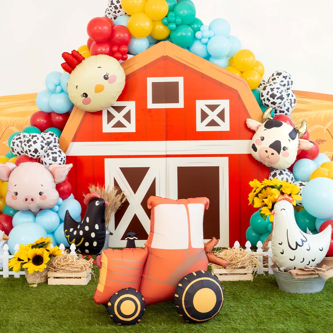 Partydeco folieballon tractor op de voorgrond van een boerderijthema feestdecoratie met ballonnen en een rode schuur.