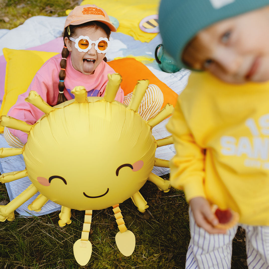 Partydeco folieballon in de vorm van een lachende zon op het gras met twee kinderen.
