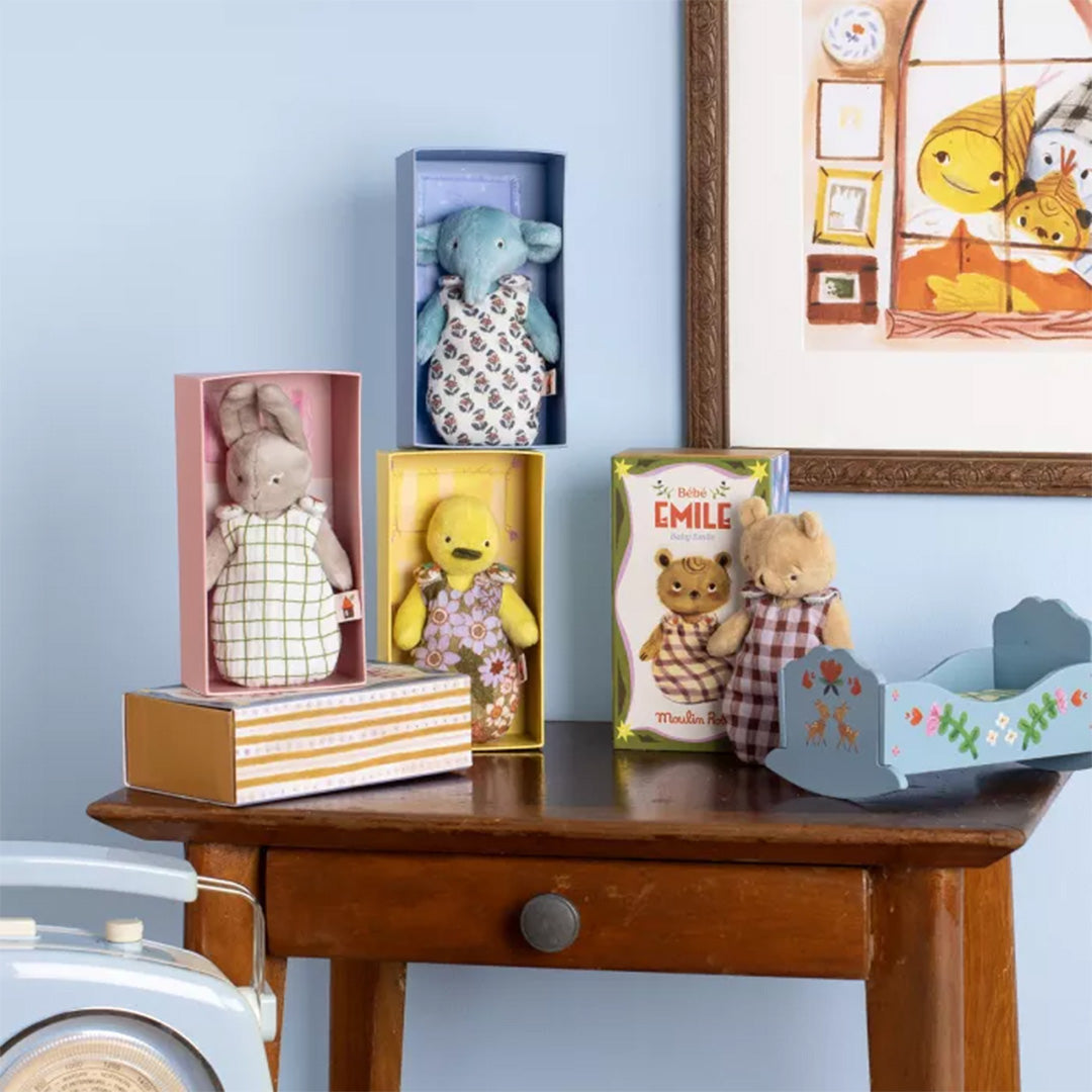 Een collectie Moulin Roty pluchen speelgoed, waaronder de blauwe olifant, een konijn en een geel figuur, op een houten tafel.
