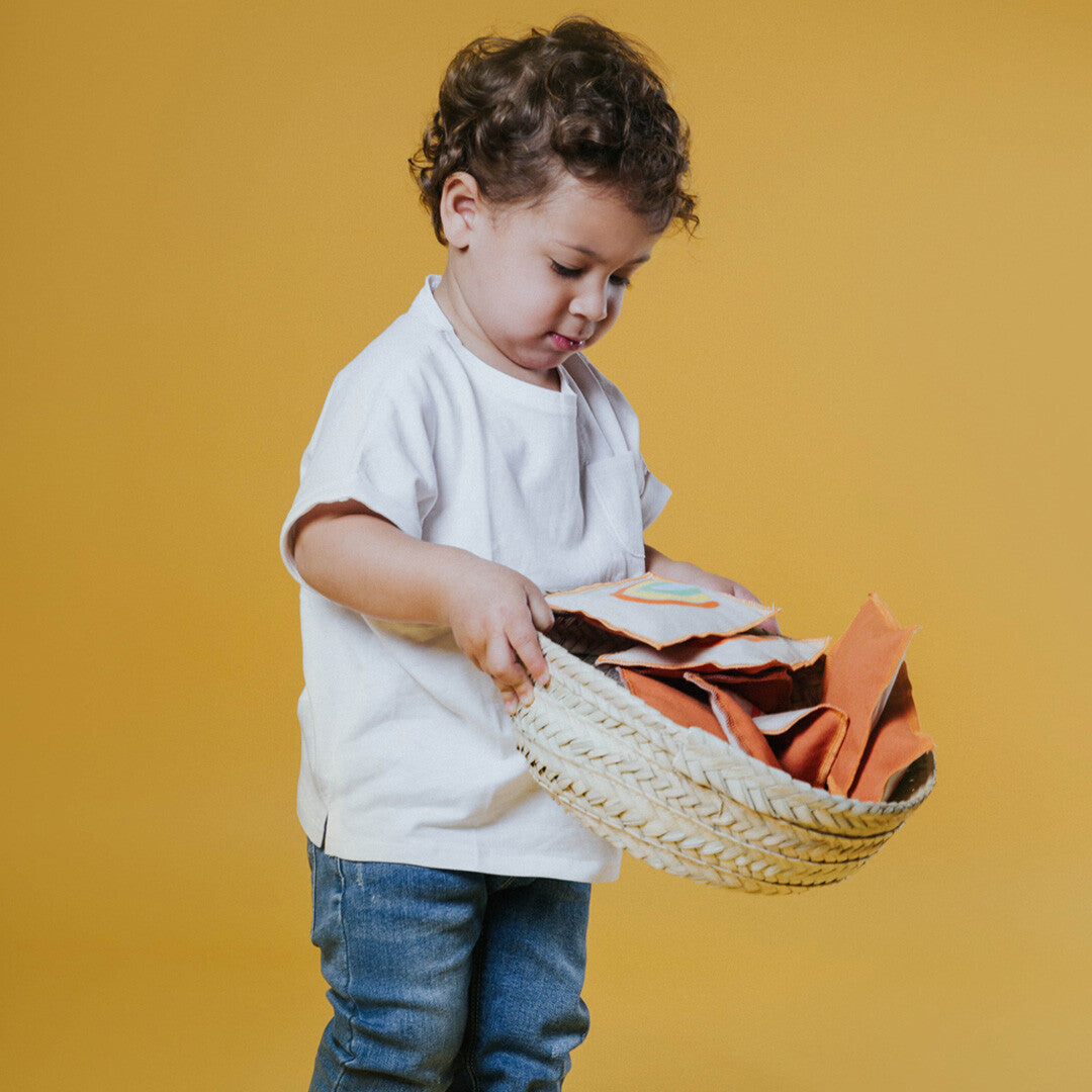 Een kind houdt een palmblad mand vast gevuld met oranje stoffen vormen.