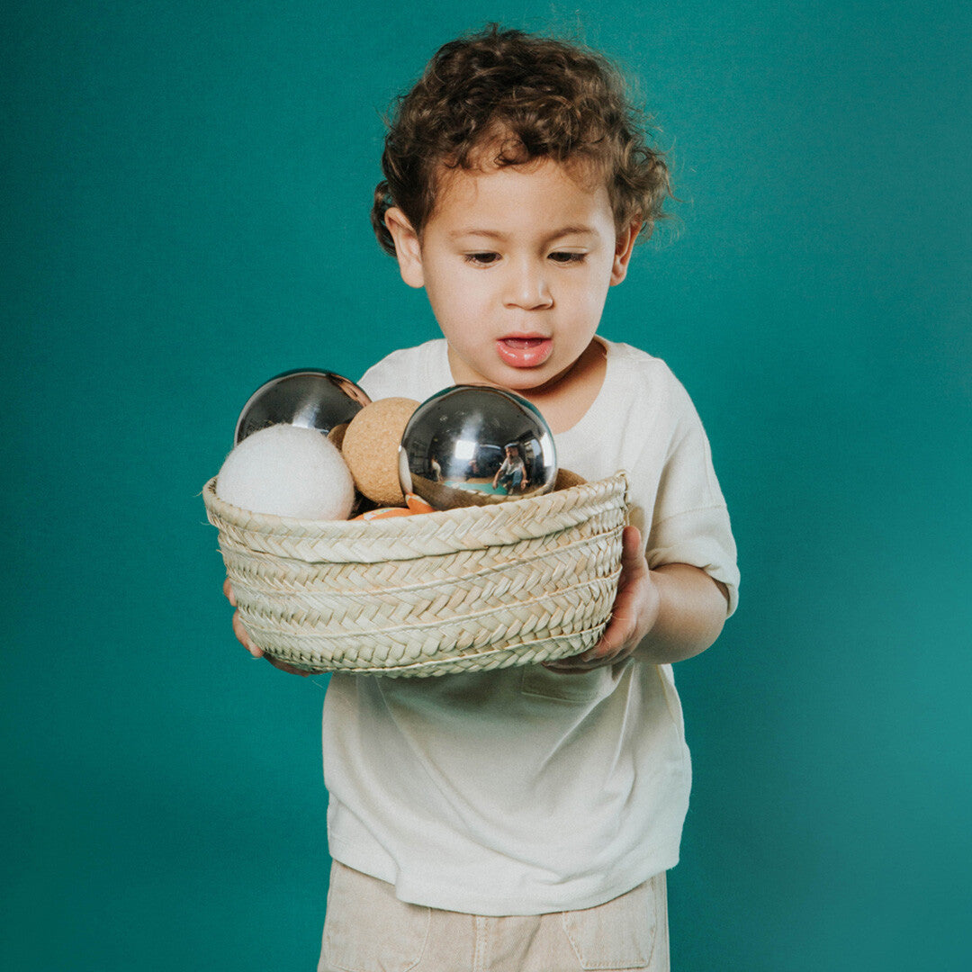 Een kind houdt een palmblad mand vast gevuld met verschillende sensorische ballen.