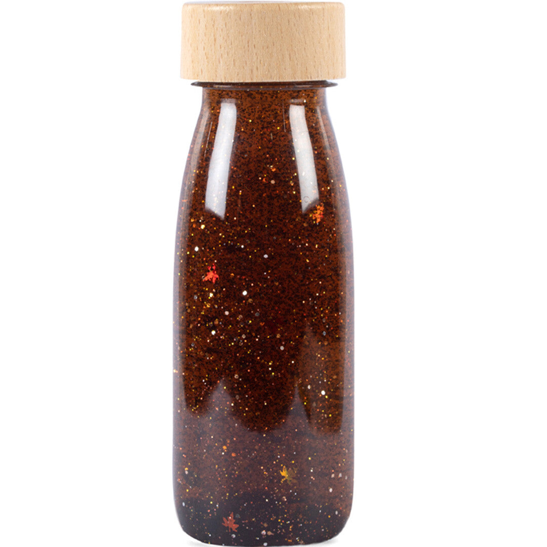 Petit Boum sensorische fles met bruine vloeistof, glitters en bladeren, afgesloten met een houten dop.