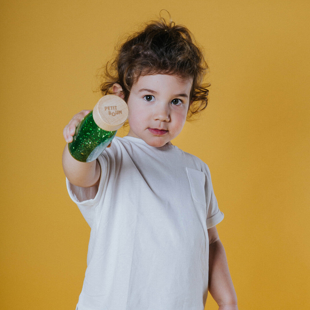 Een kind houdt de Petit Boum groene sensorische fles met glitter vast.