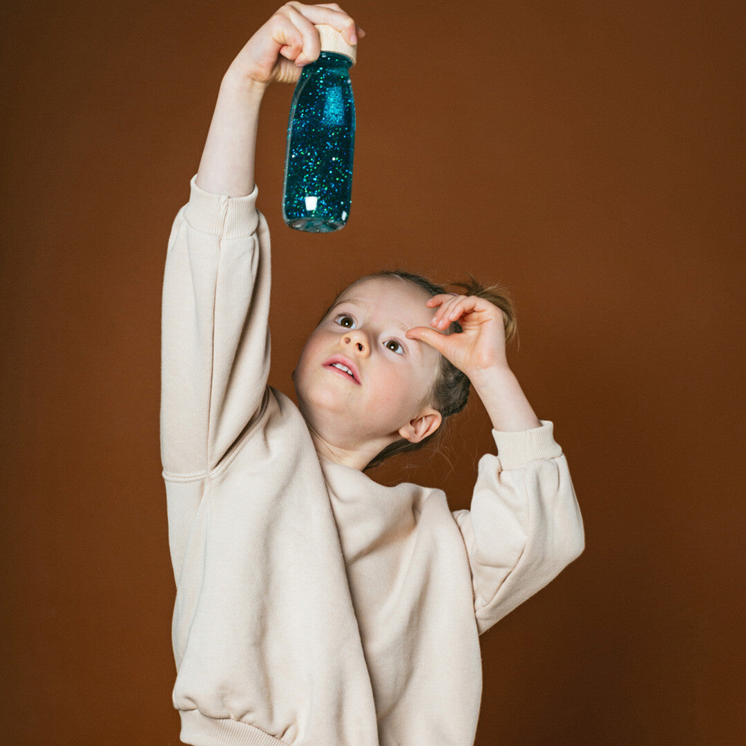 Een meisje houdt een turquoise petit boum sensorische fles omhoog.