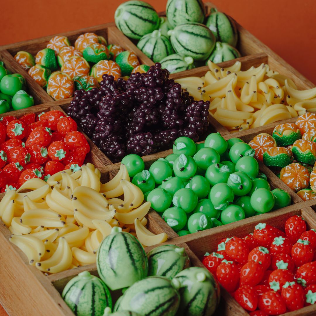 Houten sorteerbak gevuld met diverse miniatuur fruit speelgoedjes zoals watermeloenen, bananen en aardbeien.