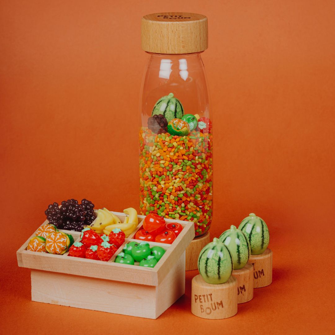 Petit Boum sensorische fles naast een houten sorteerbak met miniatuur fruit en drie watermeloen speelgoedjes op houten blokjes.