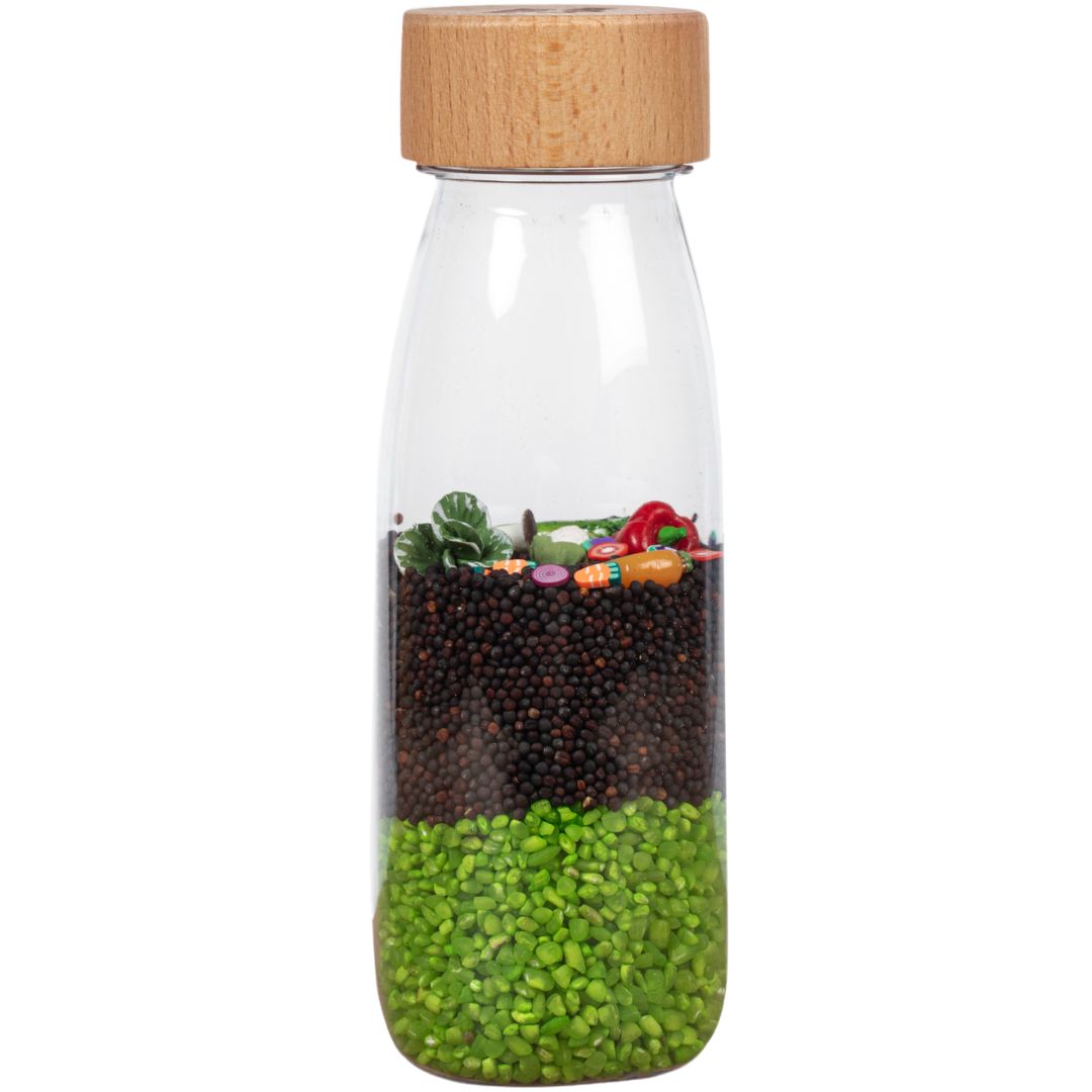 petit boum sensorische fles met houten dop, gevuld met zaden en kleine groentefiguren.