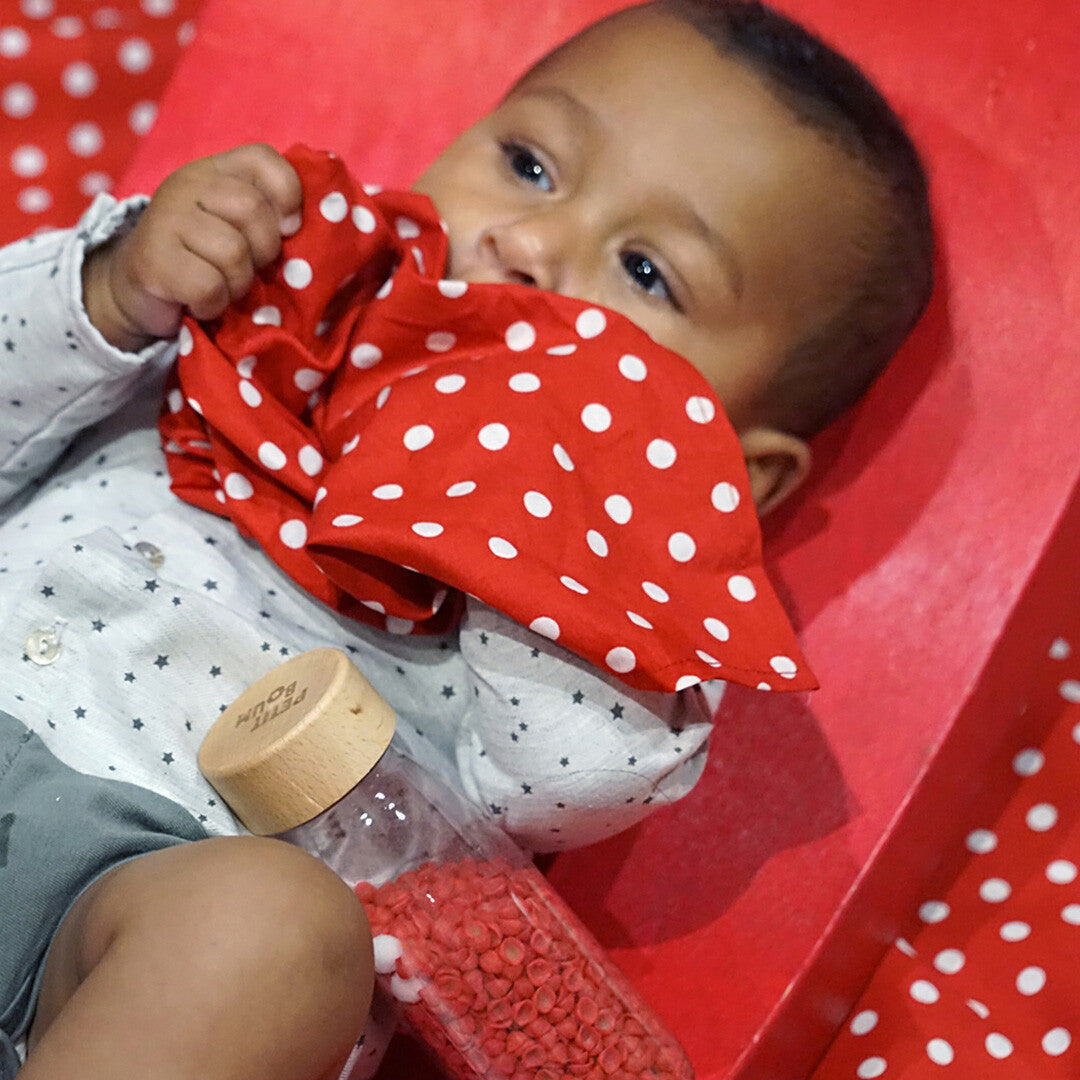 Een baby speelt met de Petit Boum sensorische fles en het rode stippendoekje.