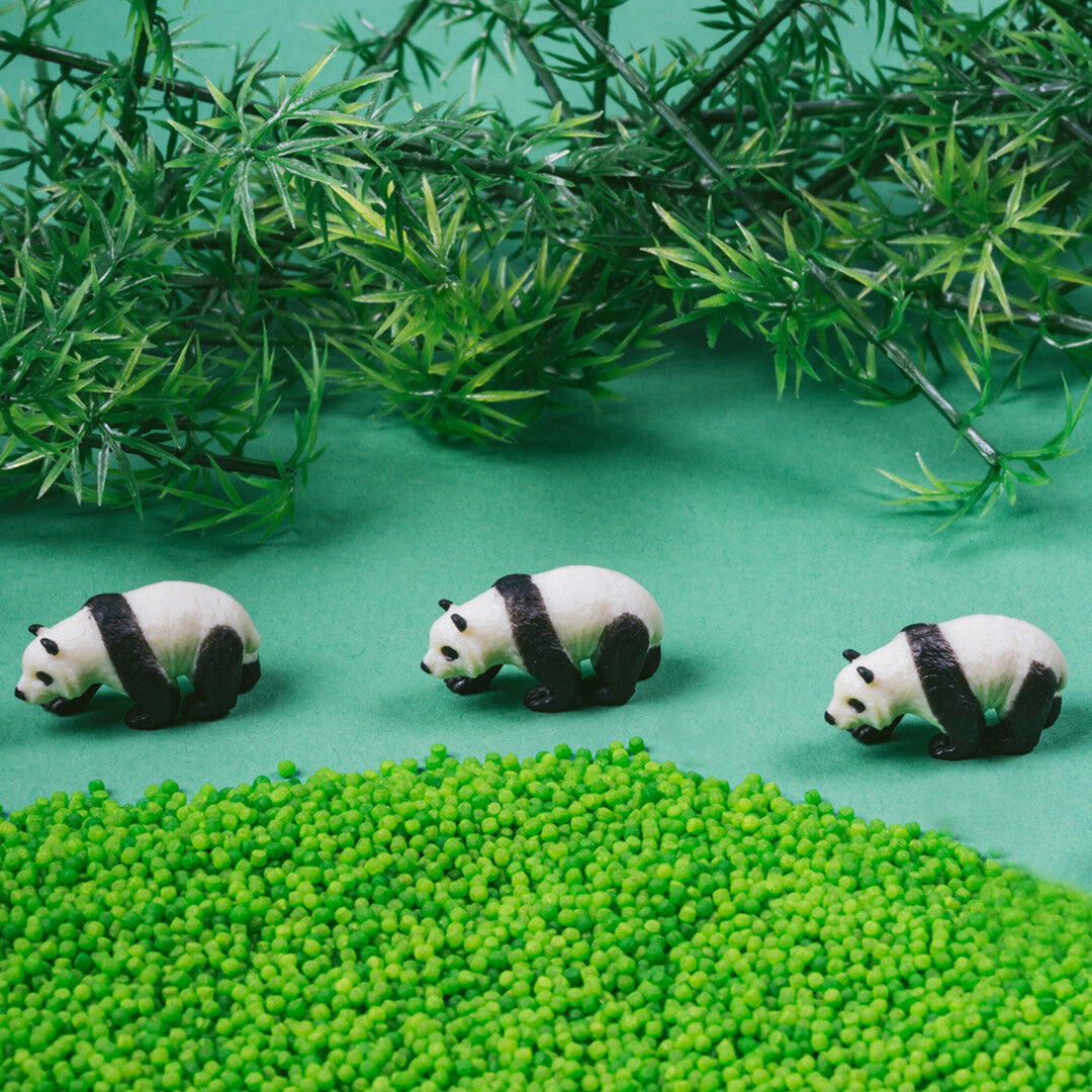 Drie kleine panda figuren op een groene ondergrond met groene korrels en planten.