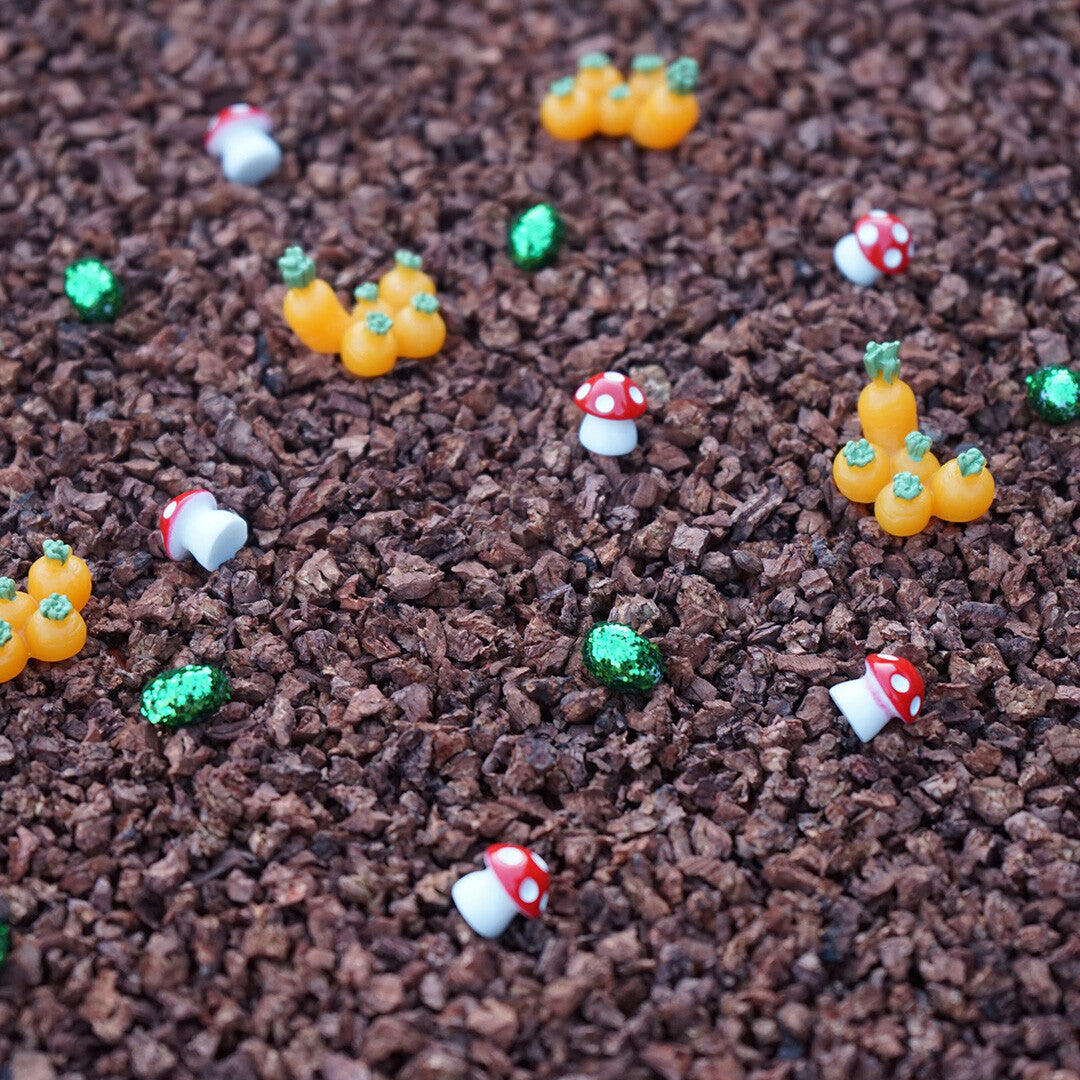 Detail van kleine oranje wortels, rode paddenstoelen en groene steentjes op een bruine ondergrond.