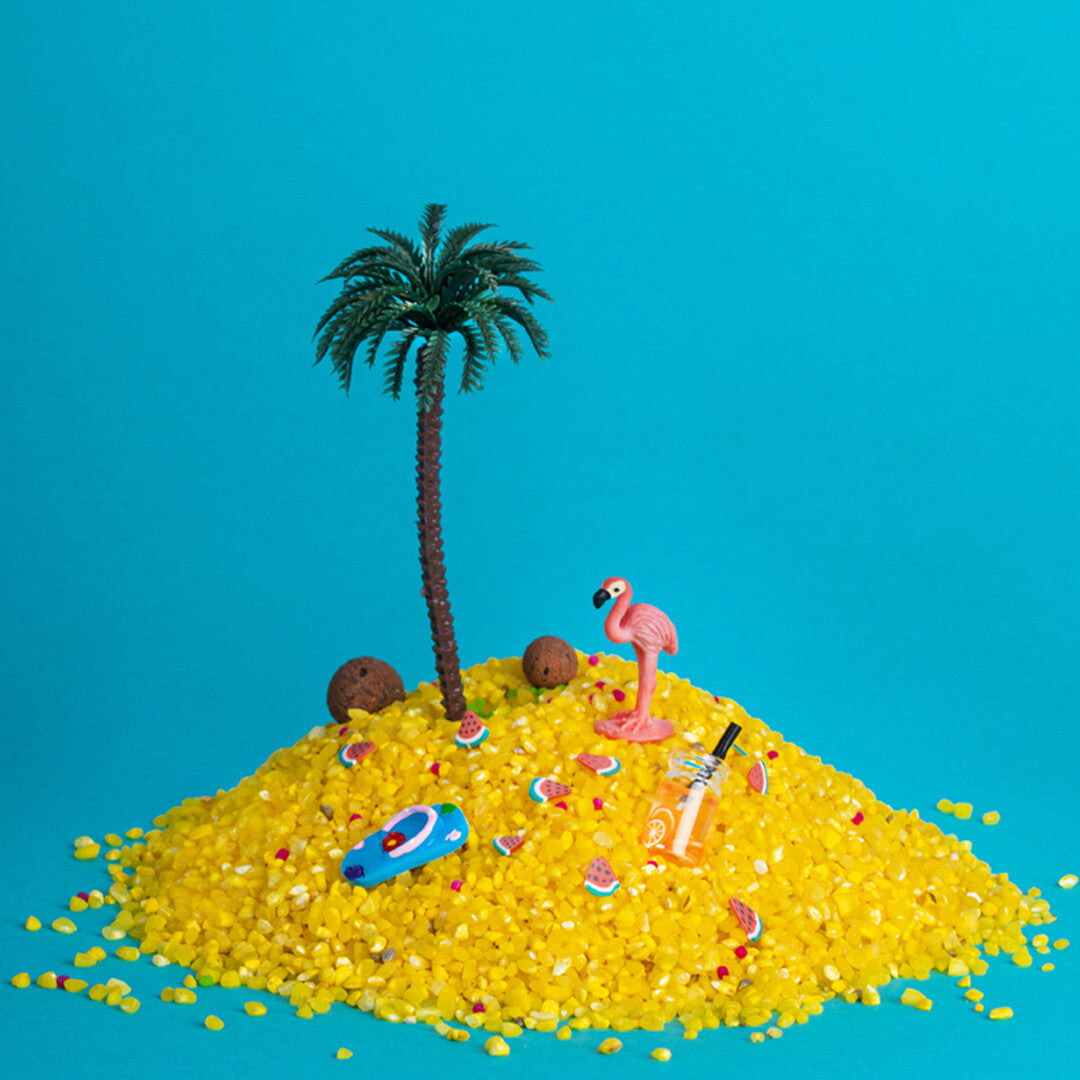 Een collectie van tropische miniaturen, waaronder een palmboom, flamingo, surfboard en drankje, op een hoop gele kralen.