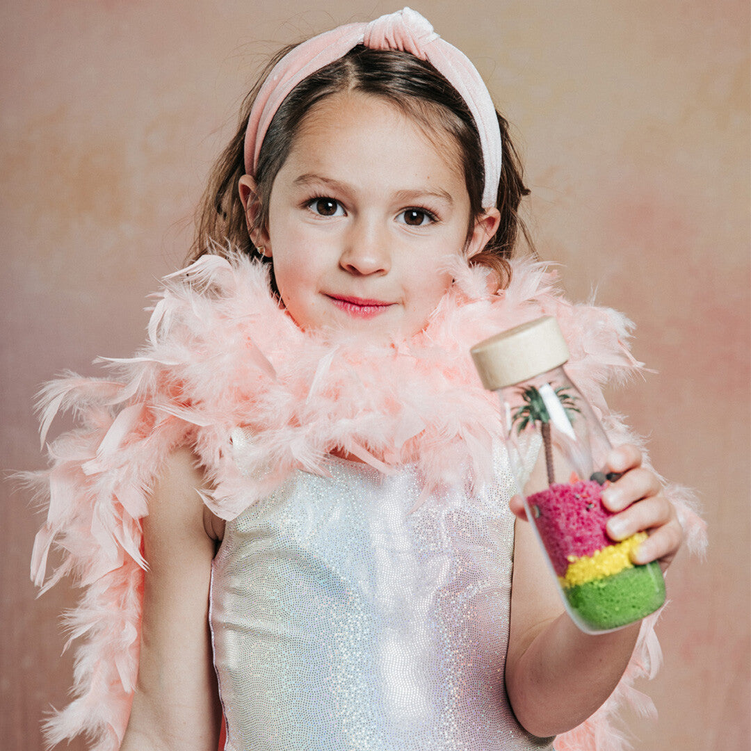Een lachend meisje met een roze boa houdt de petit boum sensorische fles met flamingo thema vast.