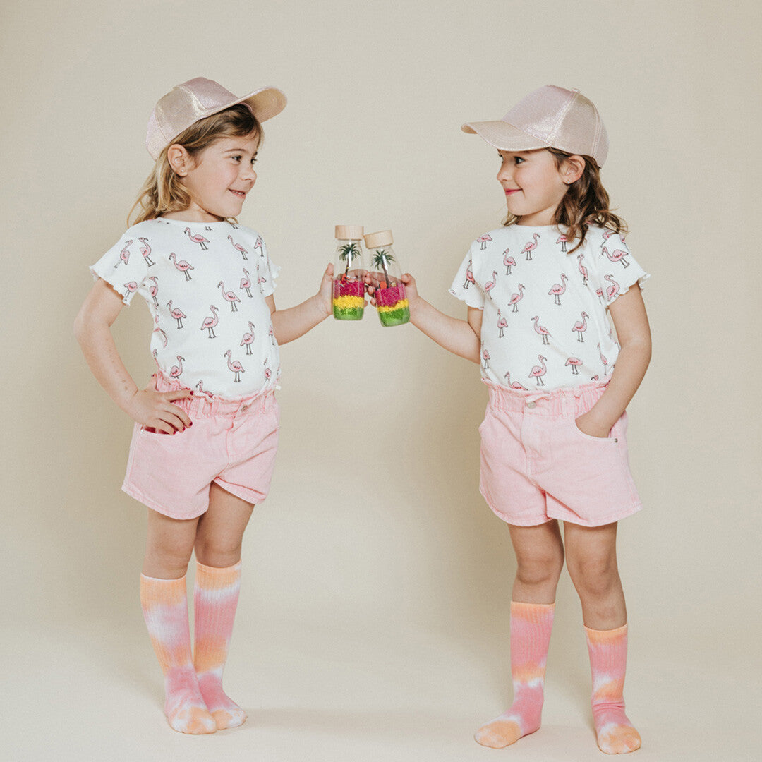 Twee meisjes in bijpassende kleding met flamingo-print houden elk een petit boum sensorische fles vast.