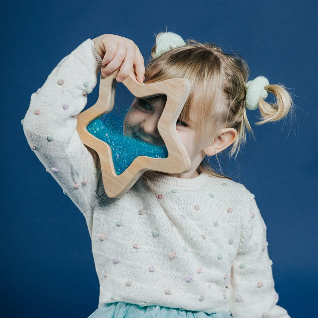 Een kind kijkt met één oog door de Petit Boum houten sensorische ster.