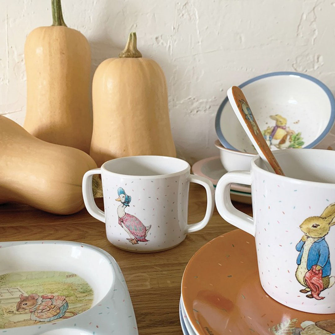 Een tafel met diverse baby- en peuterserviesstukken met figuren van Pieter Konijn en vrienden, met pompoenen op de achtergrond.