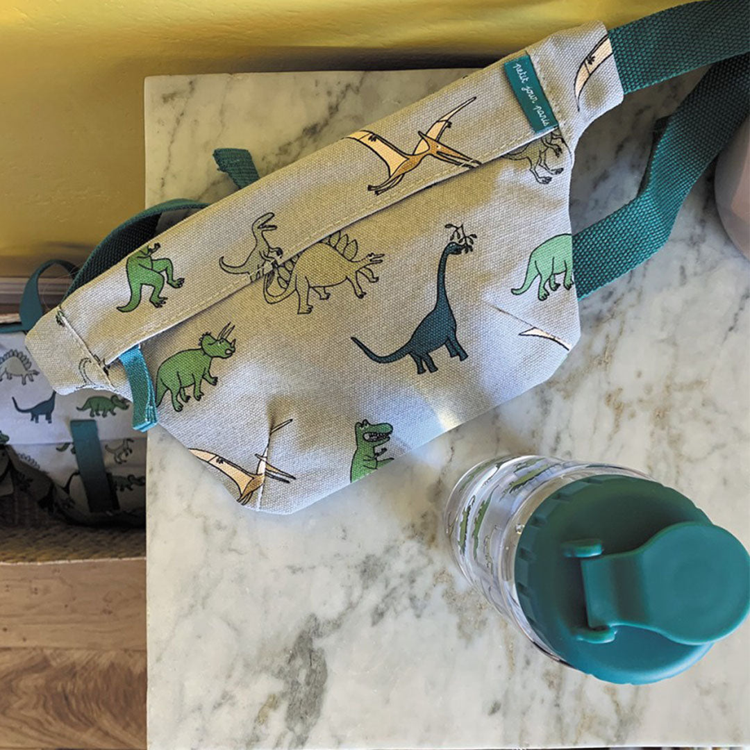 petit jour kinder drinkfles met dinosaurusprint naast een bijpassende heuptas met dezelfde dinosaurusprint.