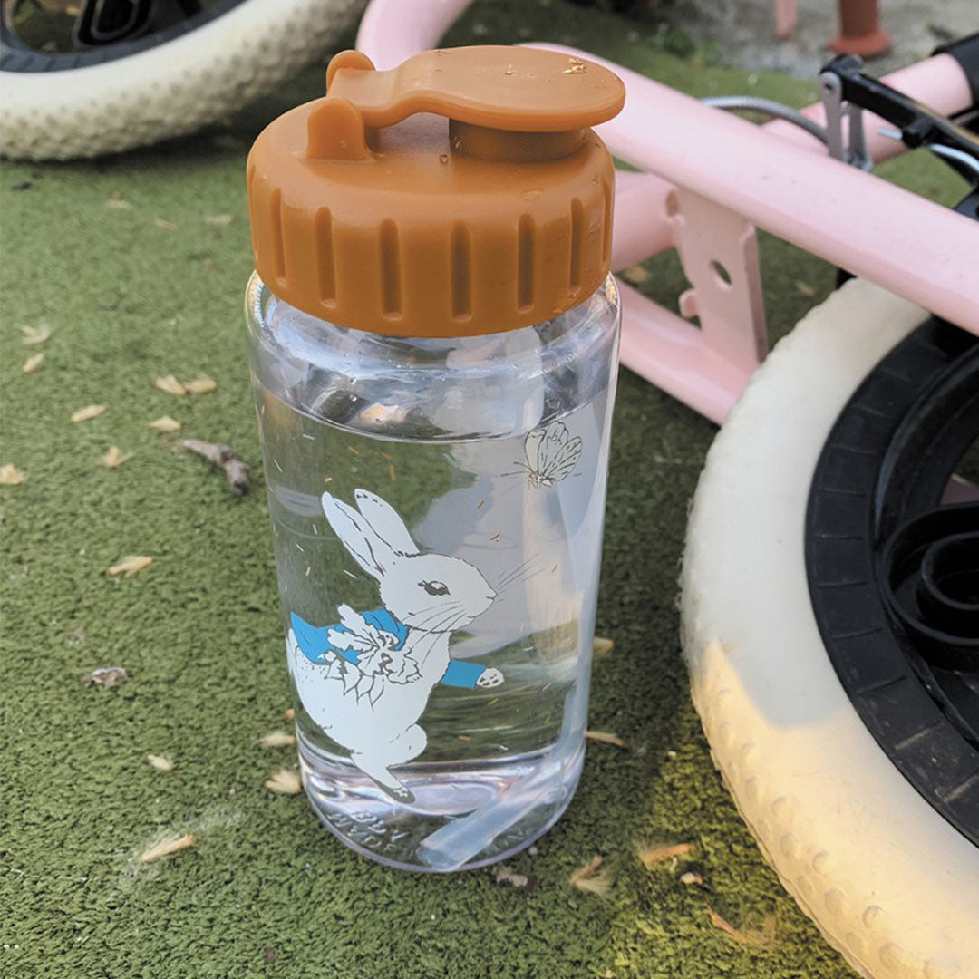 De petit jour drinkfles met Pieter Konijn illustratie staat gevuld met water op groen gras naast een fietswiel.