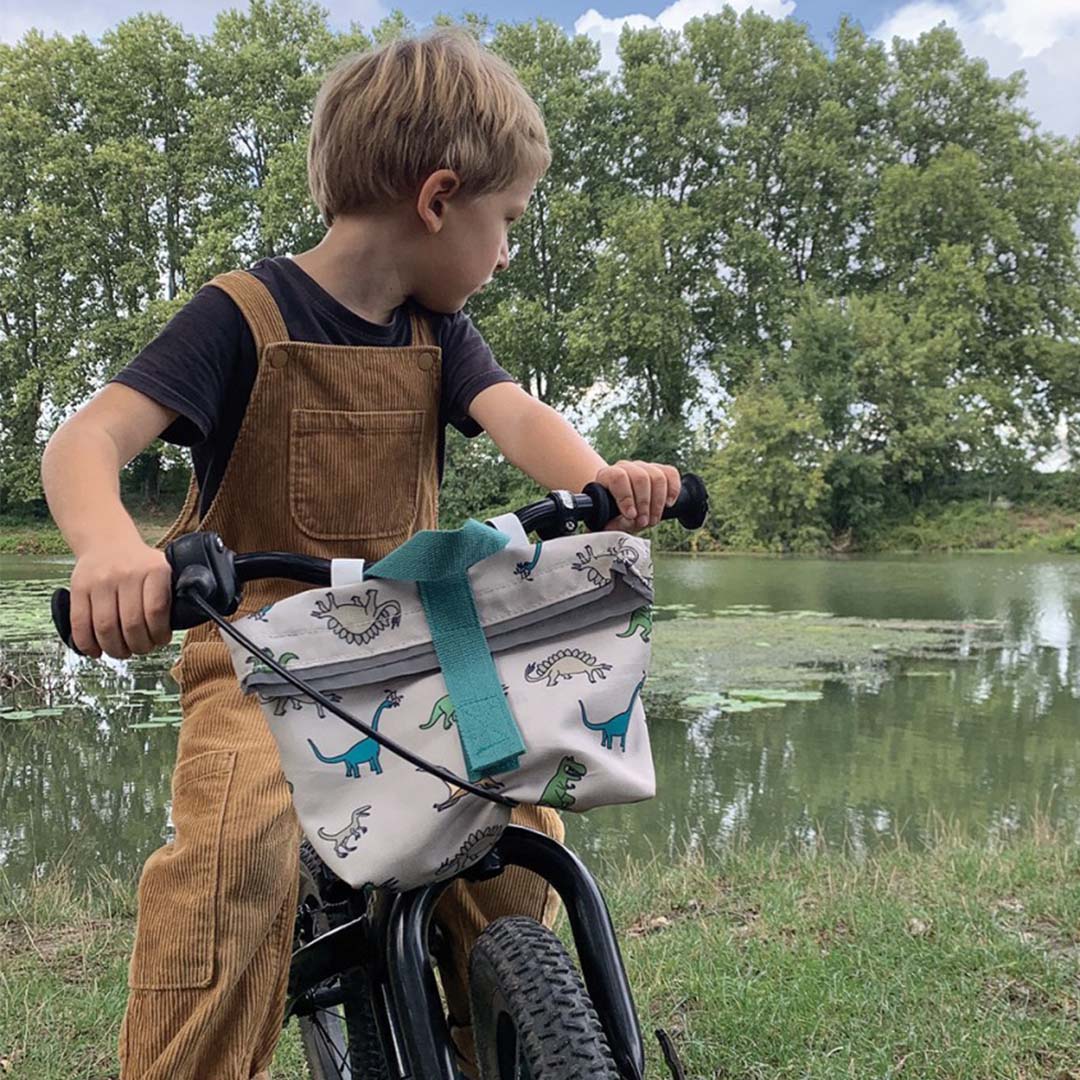 Kind op een fiets met de dinosaurus fietstas aan het stuur, bij een meer.