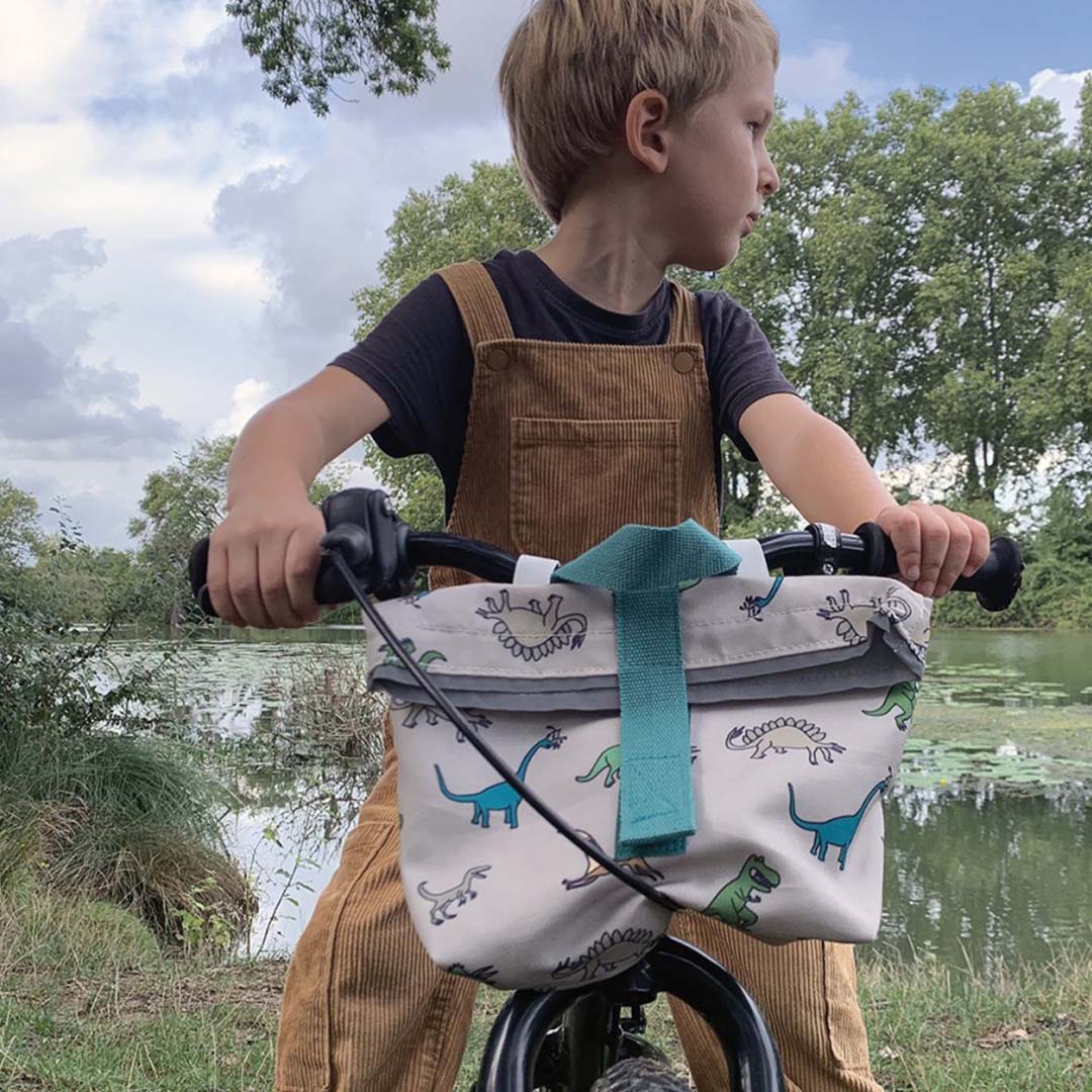 Kind op een fiets met de dinosaurus fietstas aan het stuur, met een meer op de achtergrond.