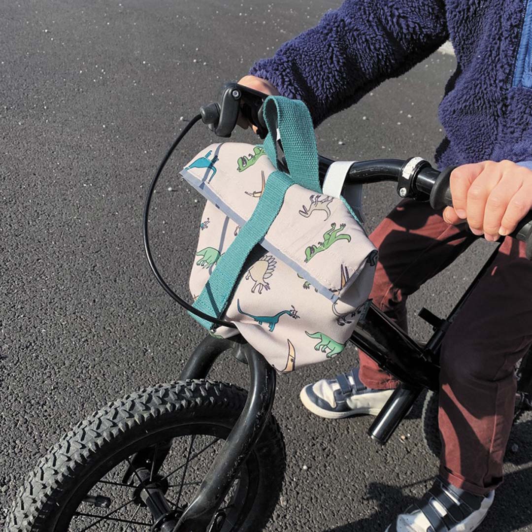 Close-up van een kind op een fiets met de dinosaurus fietstas aan het stuur.