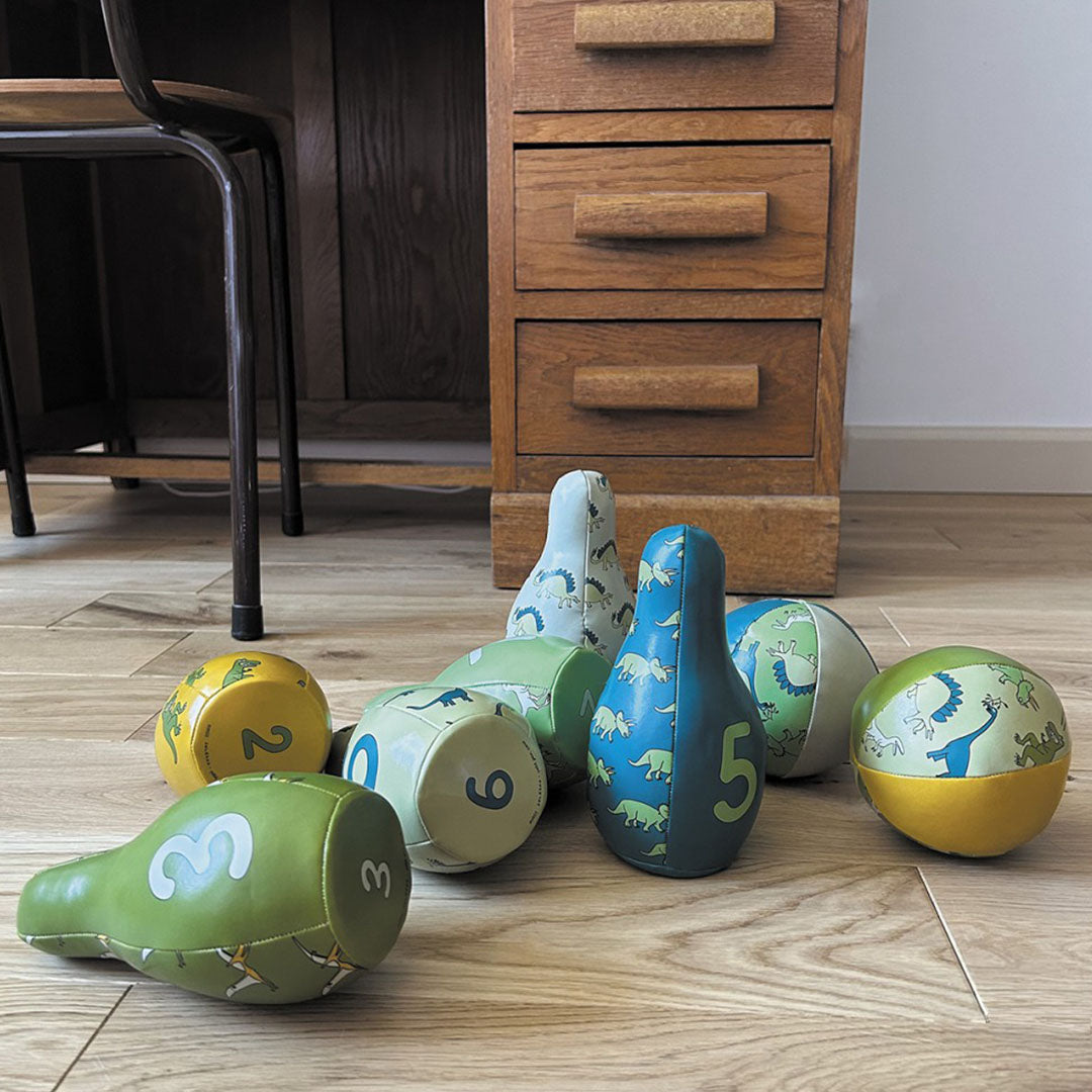 Dinosaurus kegels en ballen van het kegelspel liggen verspreid op een houten vloer.