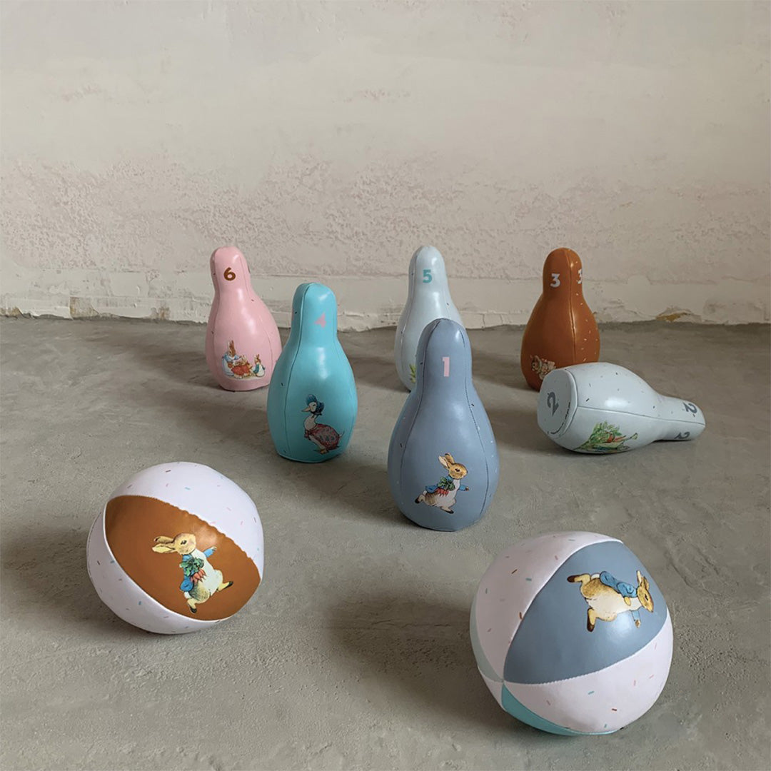 Het petit jour Pieter Konijn kegelspel op een grijze vloer, met zes kegels en drie ballen, waarvan één kegel omgevallen is.