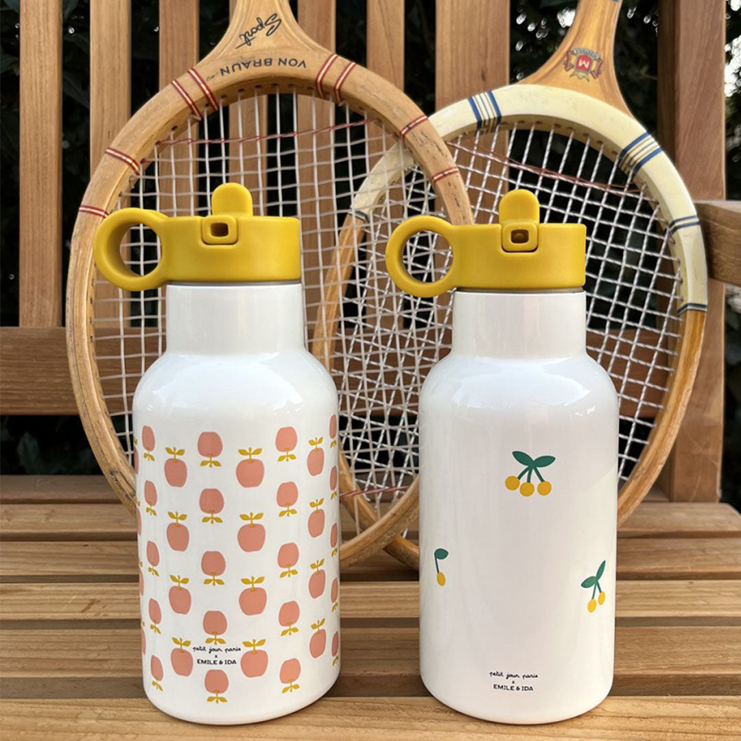 Twee witte rvs drinkflessen, één met appelpatroon en één met kersenpatroon, staan op een houten bank voor tennisrackets.