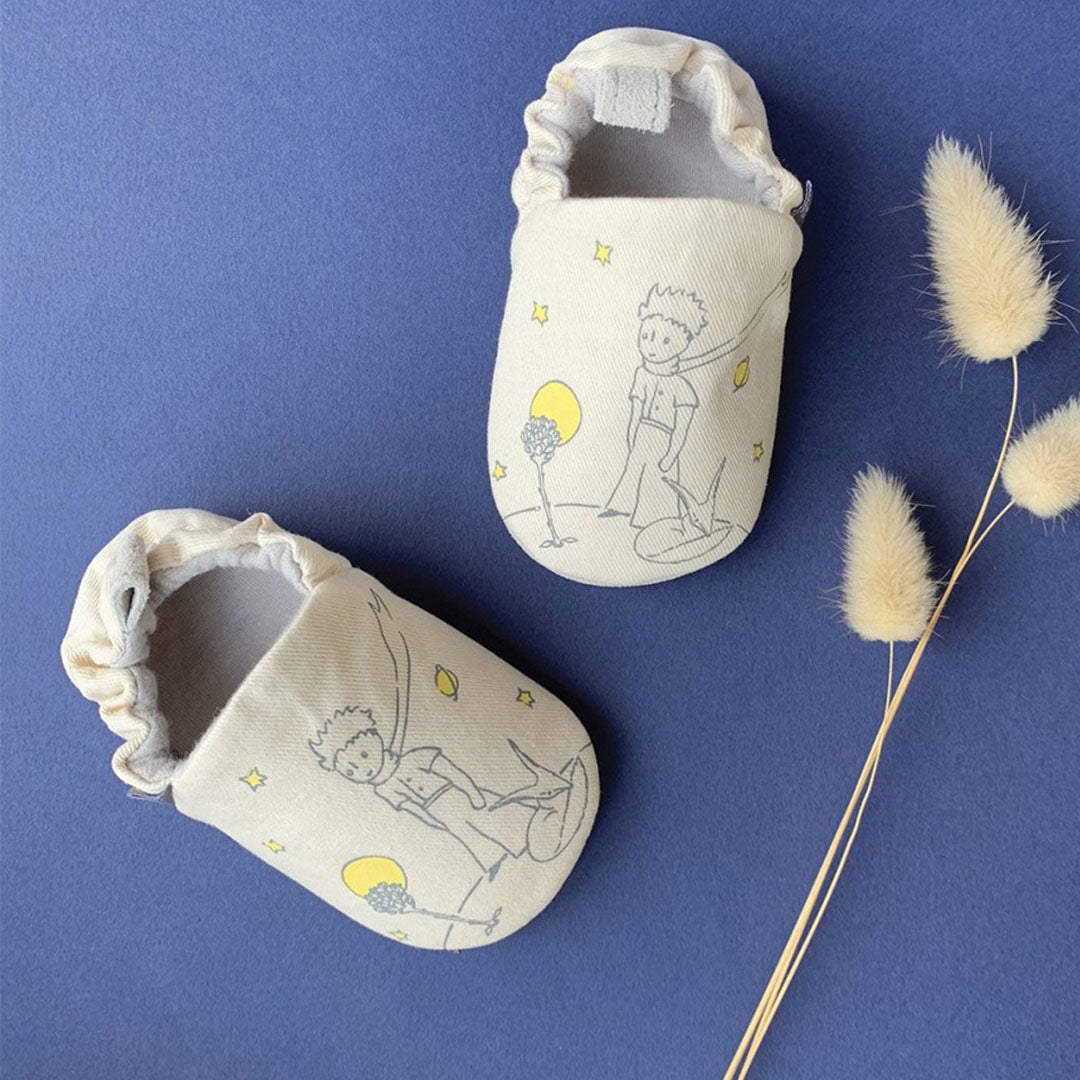 Twee beige petit jour baby schoentjes met illustraties van De Kleine Prins en de vos op een blauwe ondergrond.