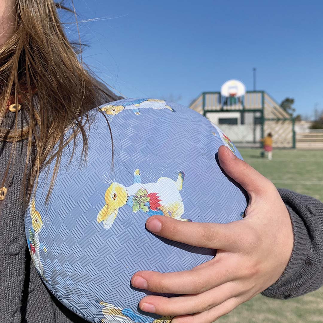 Een kind houdt de blauwe Petit Jour speelbal met Pieter Konijn figuren vast op een sportveld.