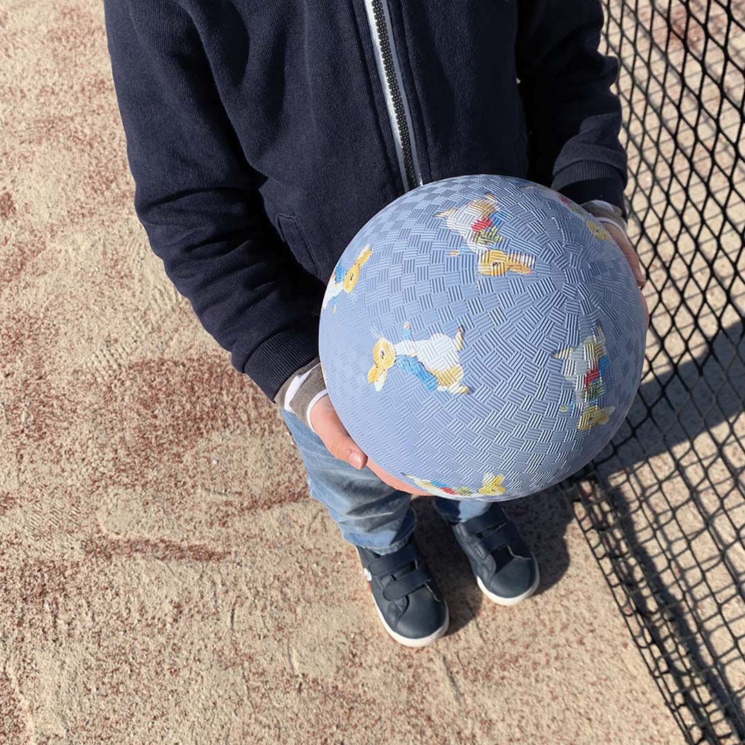 Een kind houdt de blauwe Petit Jour speelbal met Pieter Konijn figuren vast, gezien van bovenaf.