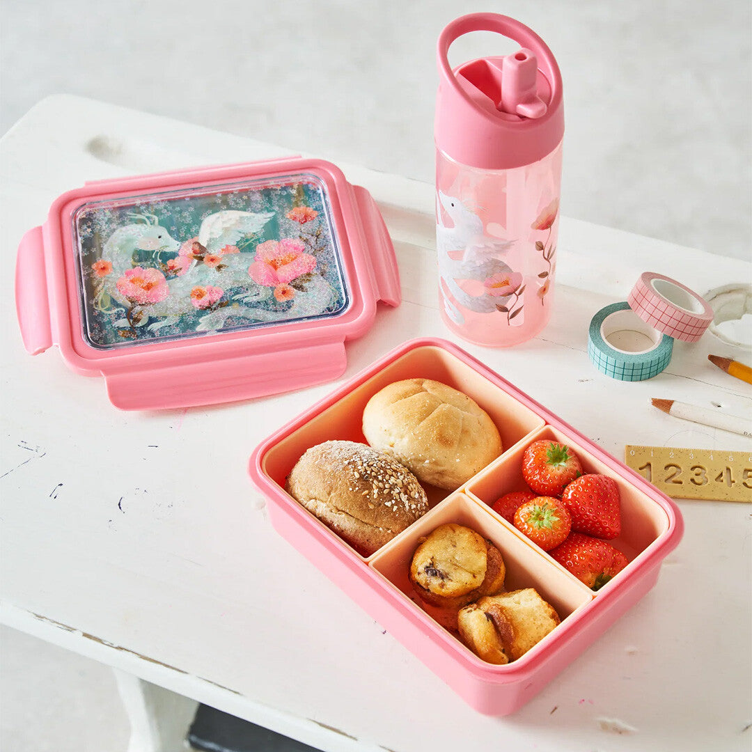 Petit Monkey roze kinderbroodtrommel gevuld met broodjes en fruit, naast een bijpassende drinkfles op een tafel.