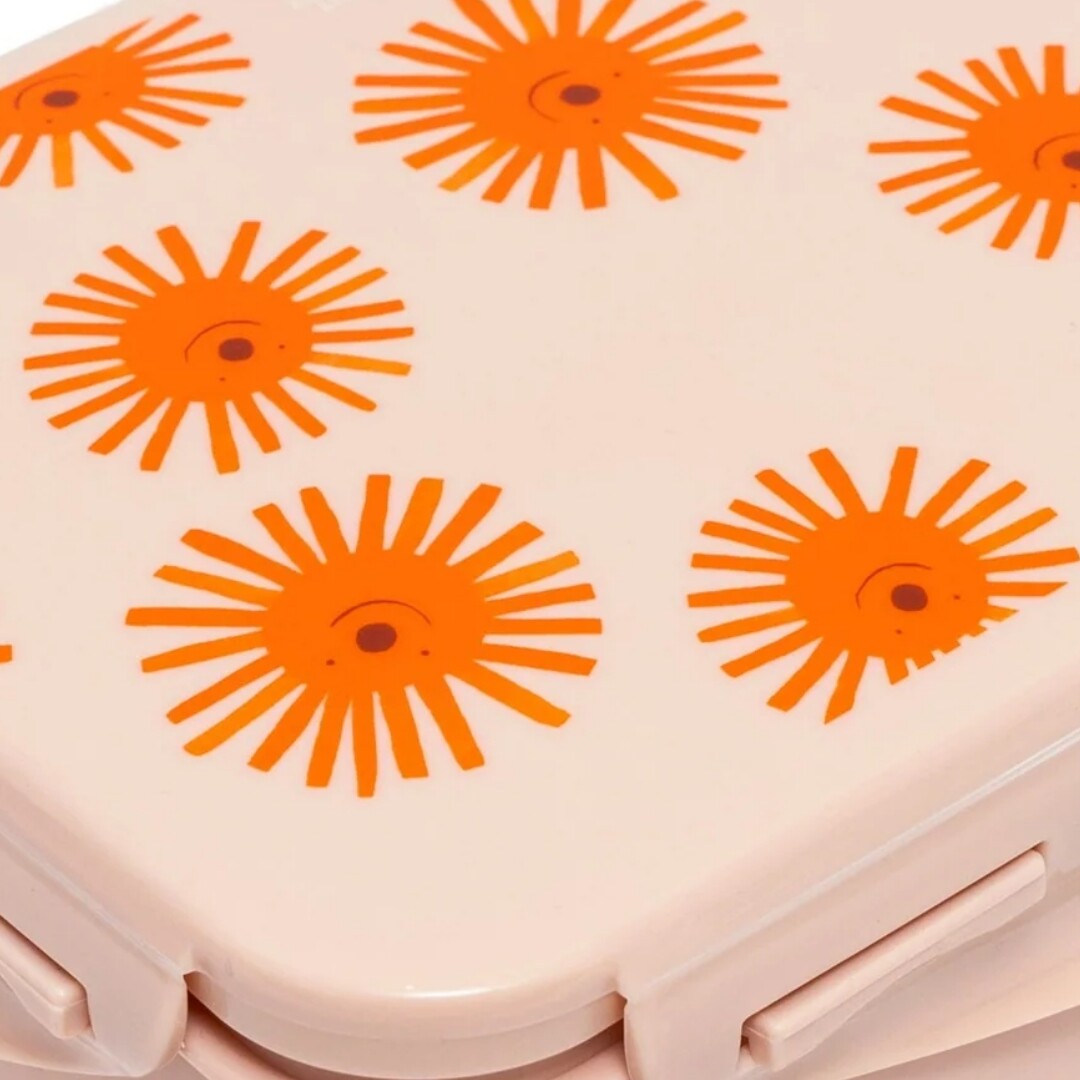 Detail van de roze deksel van een kinderbroodtrommel met oranje zonnenpatroon.