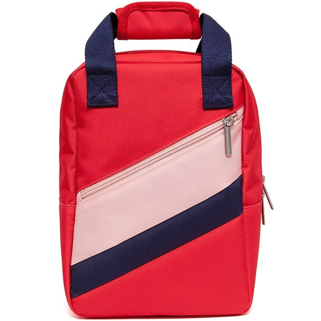 Petit Monkey peuterrugzak in rood met diagonale roze en donkerblauwe strepen aan de voorkant.