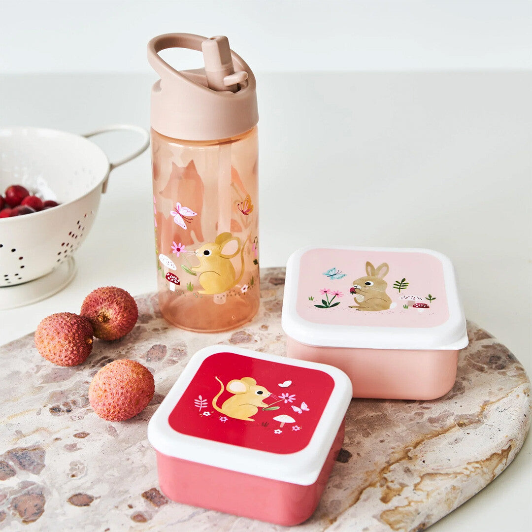 Een roze petit monkey drinkfles en twee snackdoosjes met konijn en muis op een marmeren plank.