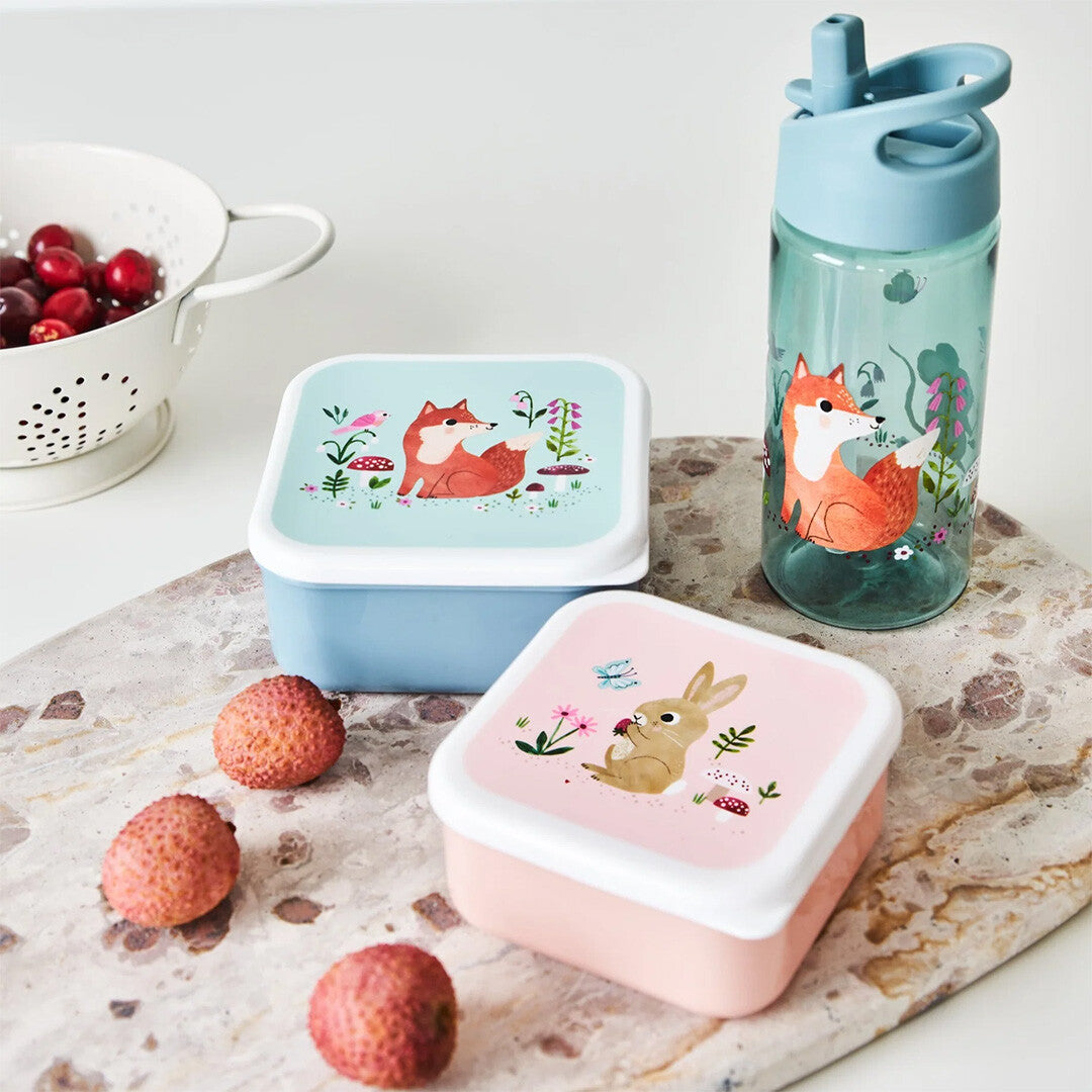 Een blauwe petit monkey drinkfles en twee snackdoosjes met vos en konijn op een marmeren plank.