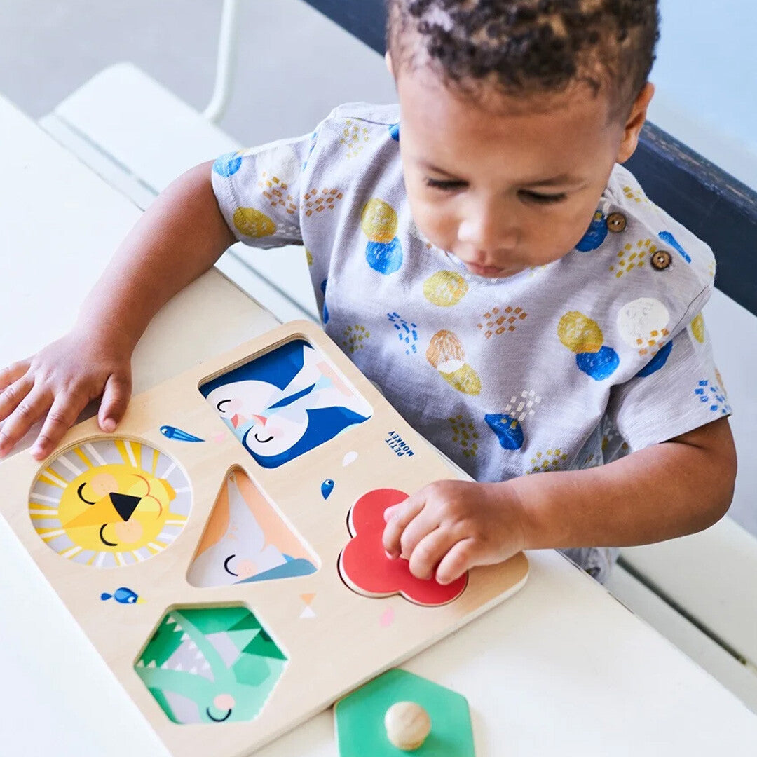 Een kind speelt met de Petit Monkey houten vormenpuzzel 'One day at the Zoo' met dierengezichten.