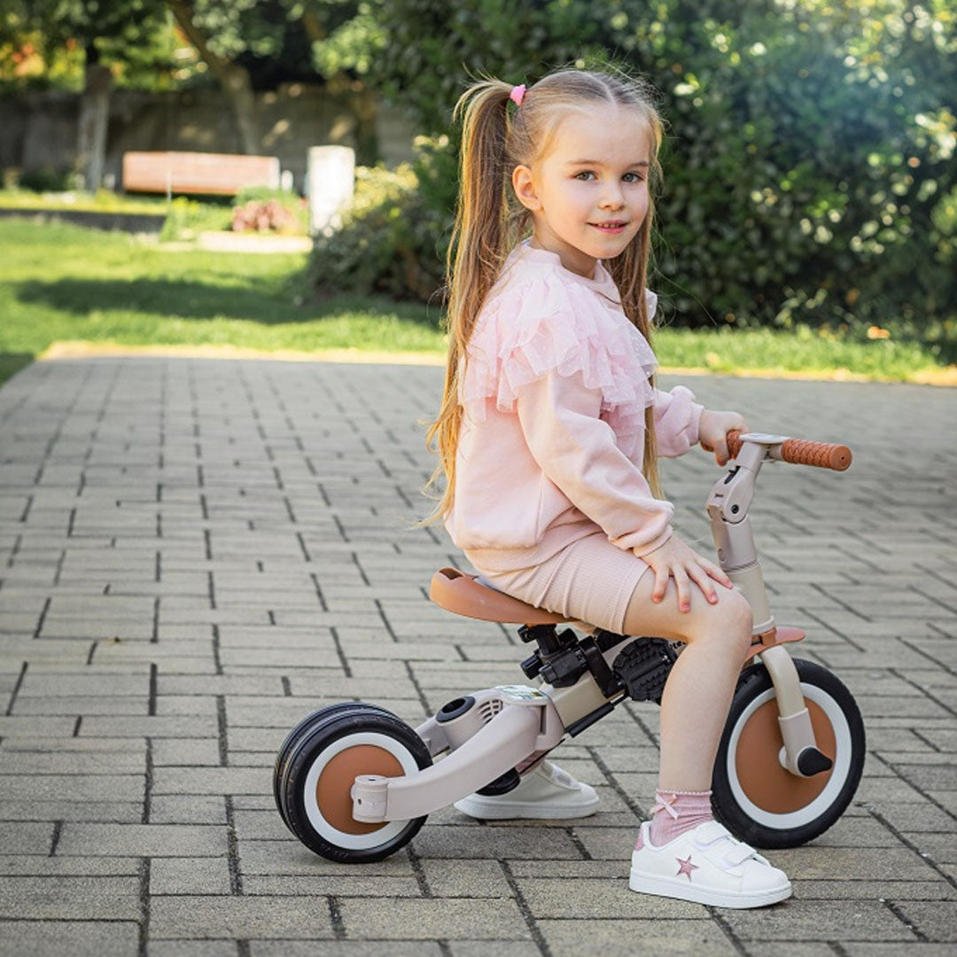 Een meisje zit op de Petite&Mars 5-in-1 kinderfiets in driewielerstand op een pad in de tuin.