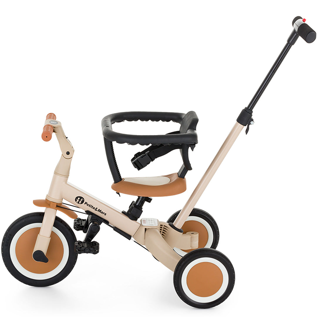 Petite&Mars 5-in-1 kinderfiets in desert sand kleur, geconfigureerd als driewieler met duwstang en veiligheidsbeugel.
