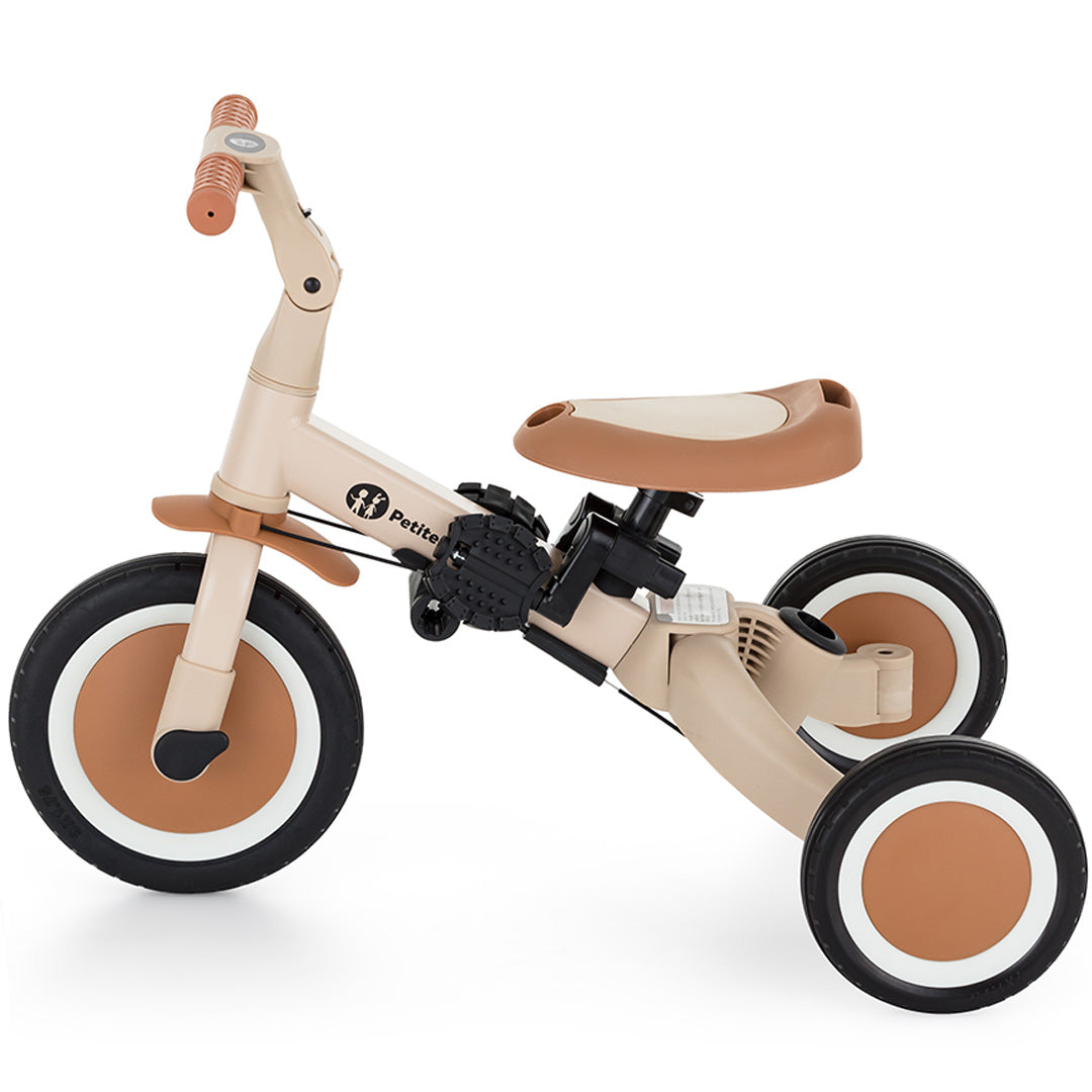 Petite&Mars 5-in-1 kinderfiets in desert sand kleur, geconfigureerd als driewieler met pedalen en veiligheidsbeugel, van links gezien.