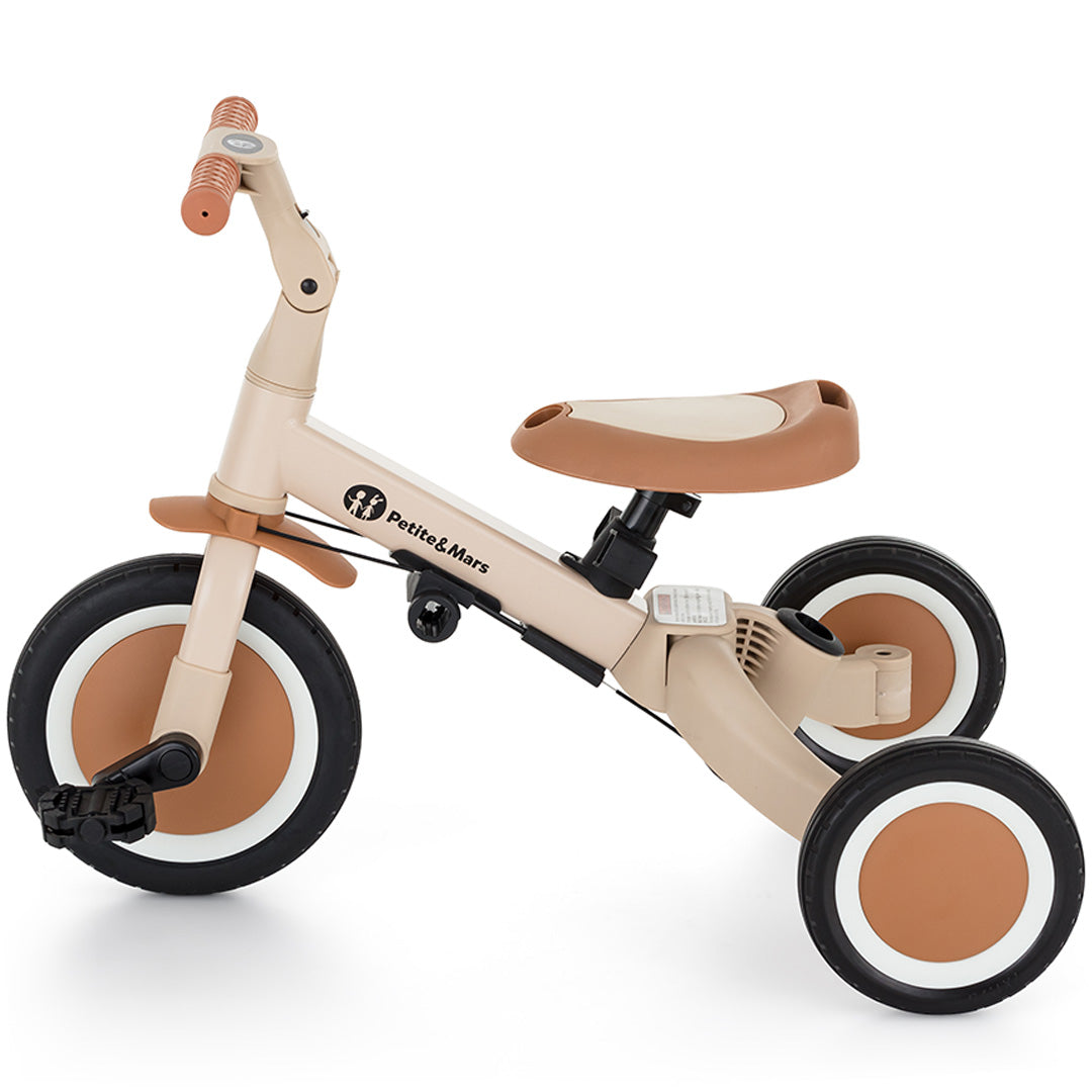 Petite&Mars 5-in-1 kinderfiets in desert sand kleur, geconfigureerd als driewieler met pedalen, van links gezien.