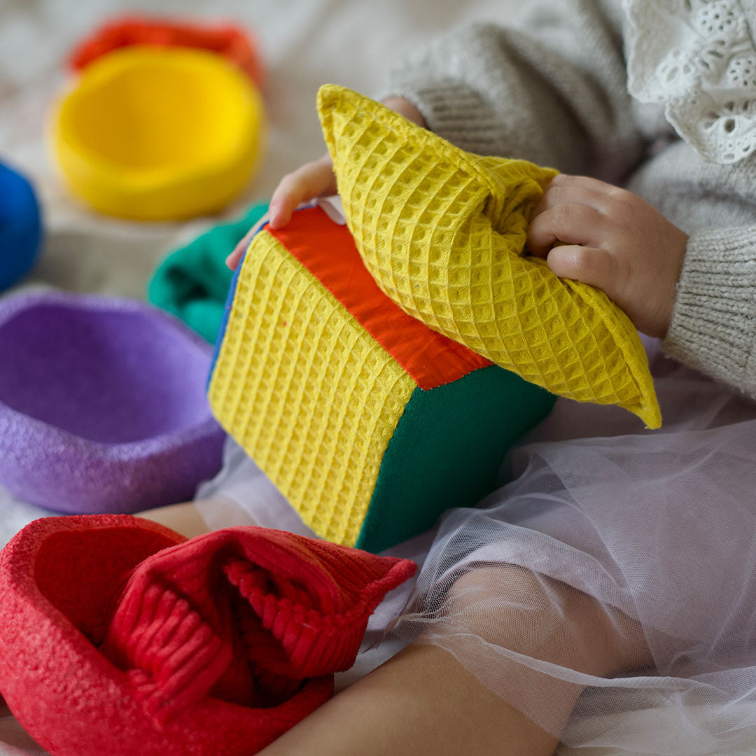Kinderhanden pakken een gele textuurstof van een veelkleurige stoffen dobbelsteen.