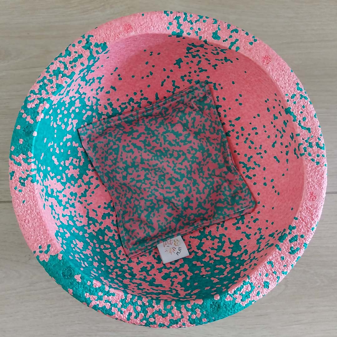 Een pit and play pittenzakje met roze en groen abstract patroon ligt in een bijpassende roze en groene speelkom.