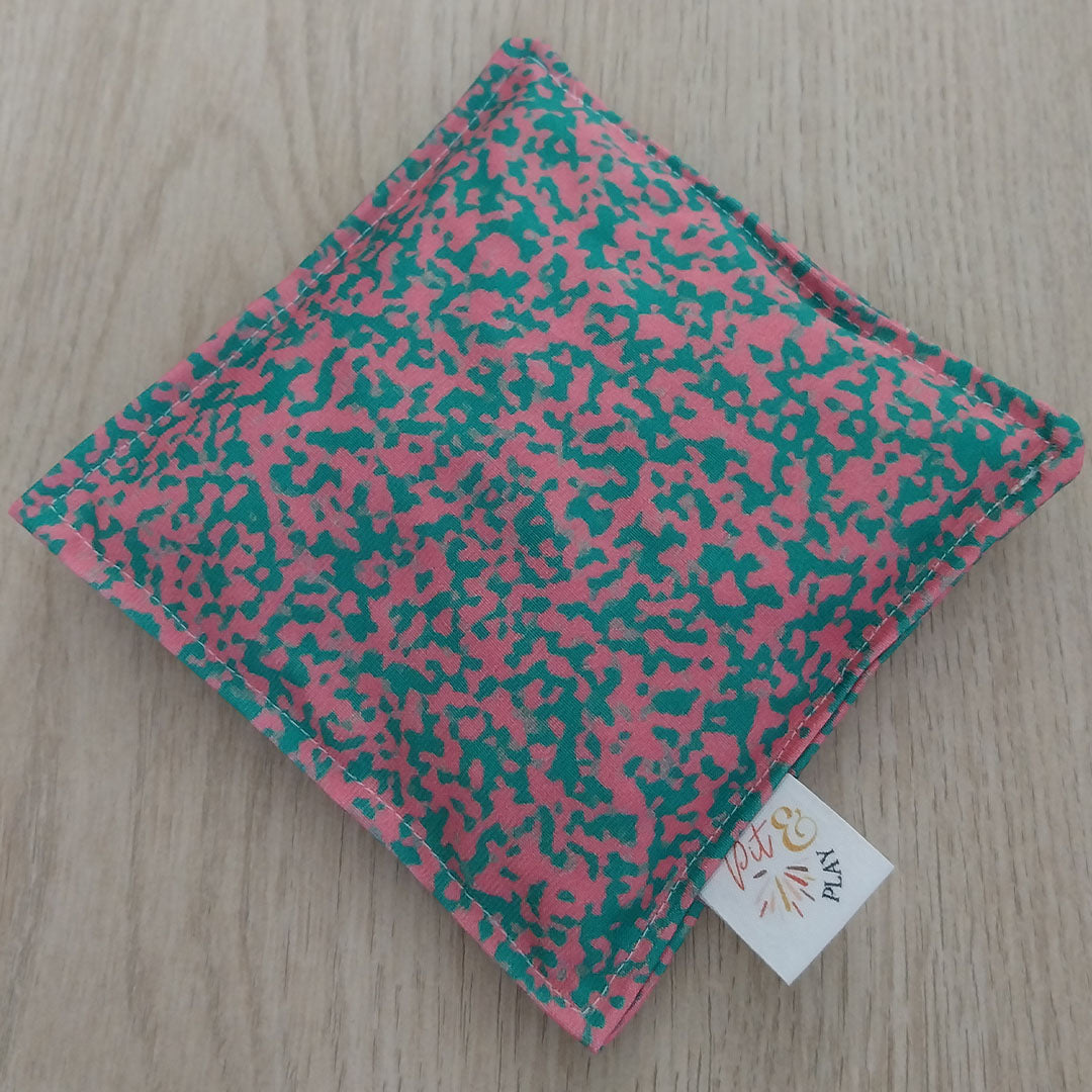 Een pit and play pittenzakje met roze en groen abstract patroon ligt schuin op een houten ondergrond.