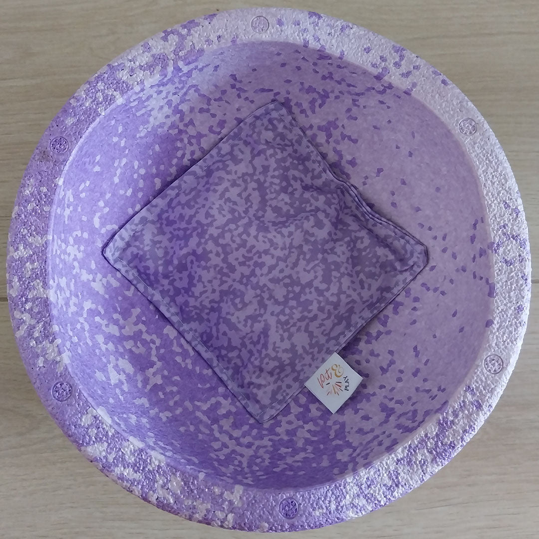 Een paars pit & play pittenzakje met textuurpatroon in een bijpassende paarse kom, van bovenaf gezien.