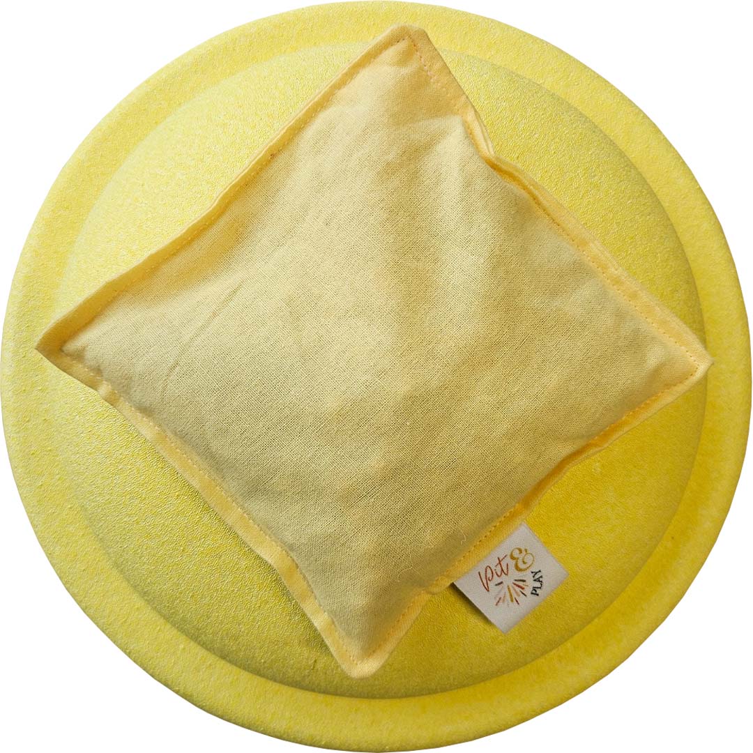 Een pastel geel pittenzakje, sensorisch speelgoed, ligt van bovenaf gezien op een ronde gele ondergrond.