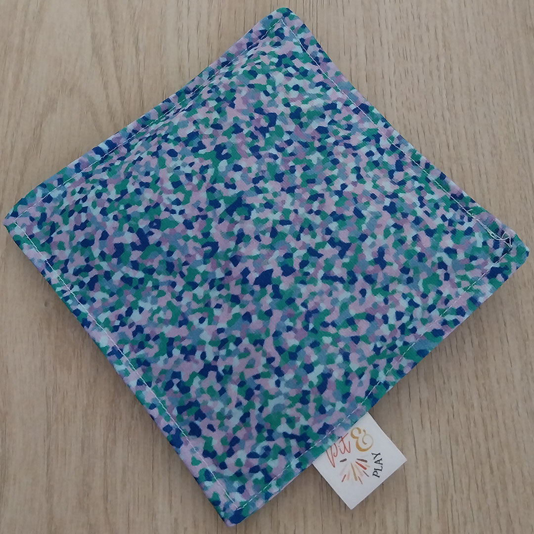 Bovenaanzicht van een pit and play pittenzakje met veelkleurig abstract stippenpatroon op een houten ondergrond.