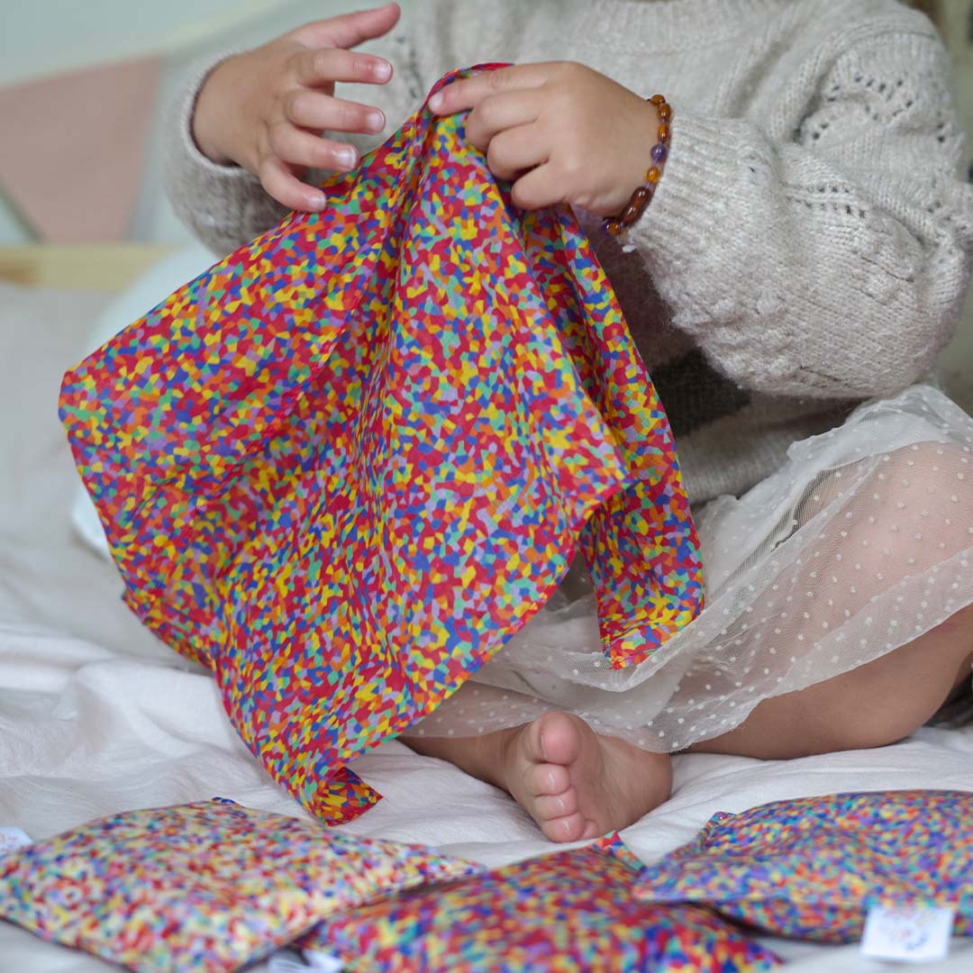 Een kind houdt een veelkleurige pit and play speeldoek met confetti patroon vast.
