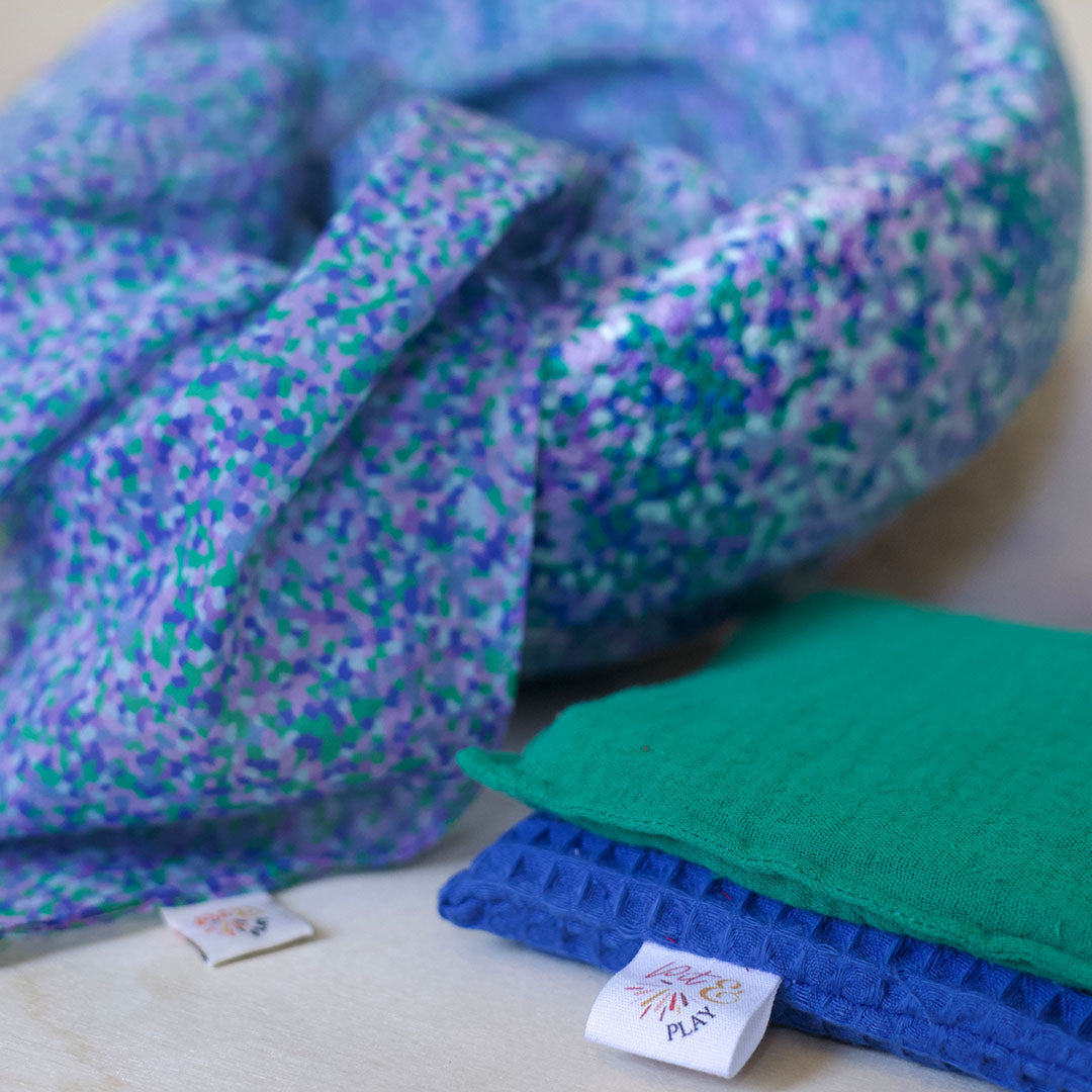 pit and play speeldoek met paars en groen puntenpatroon, met een groen en een blauw stoffen lapje ernaast.